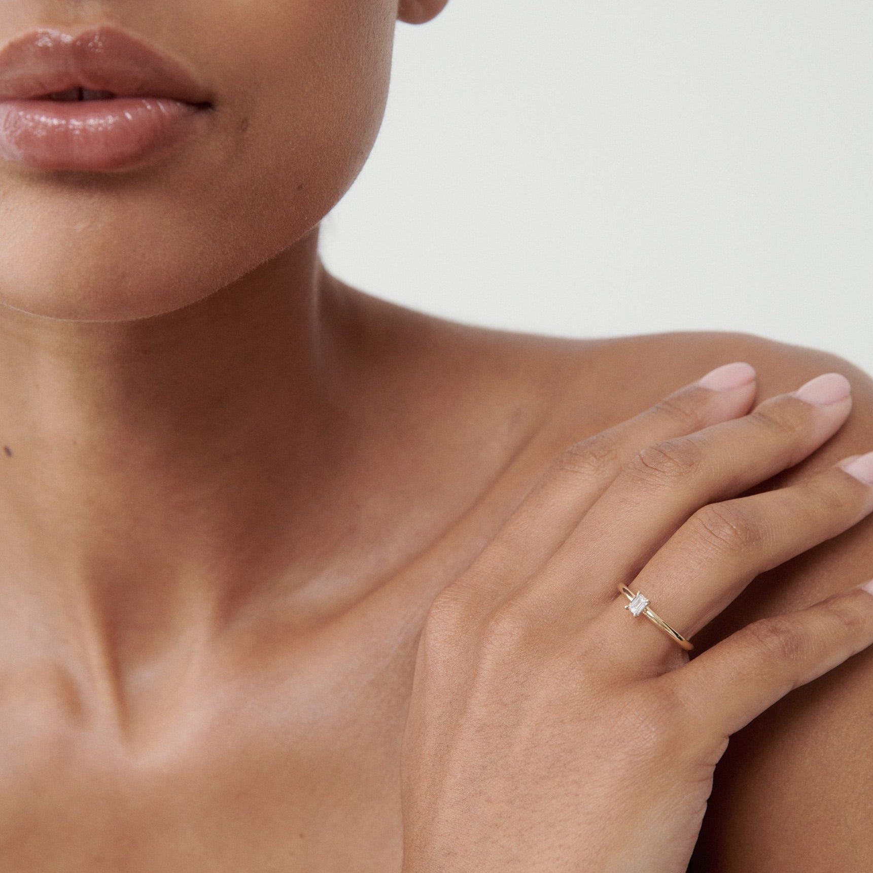 Close-up of a person wearing a minimalist gold ring with a baguette-cut diamond on their finger. Luxurious and elegant jewellery style.