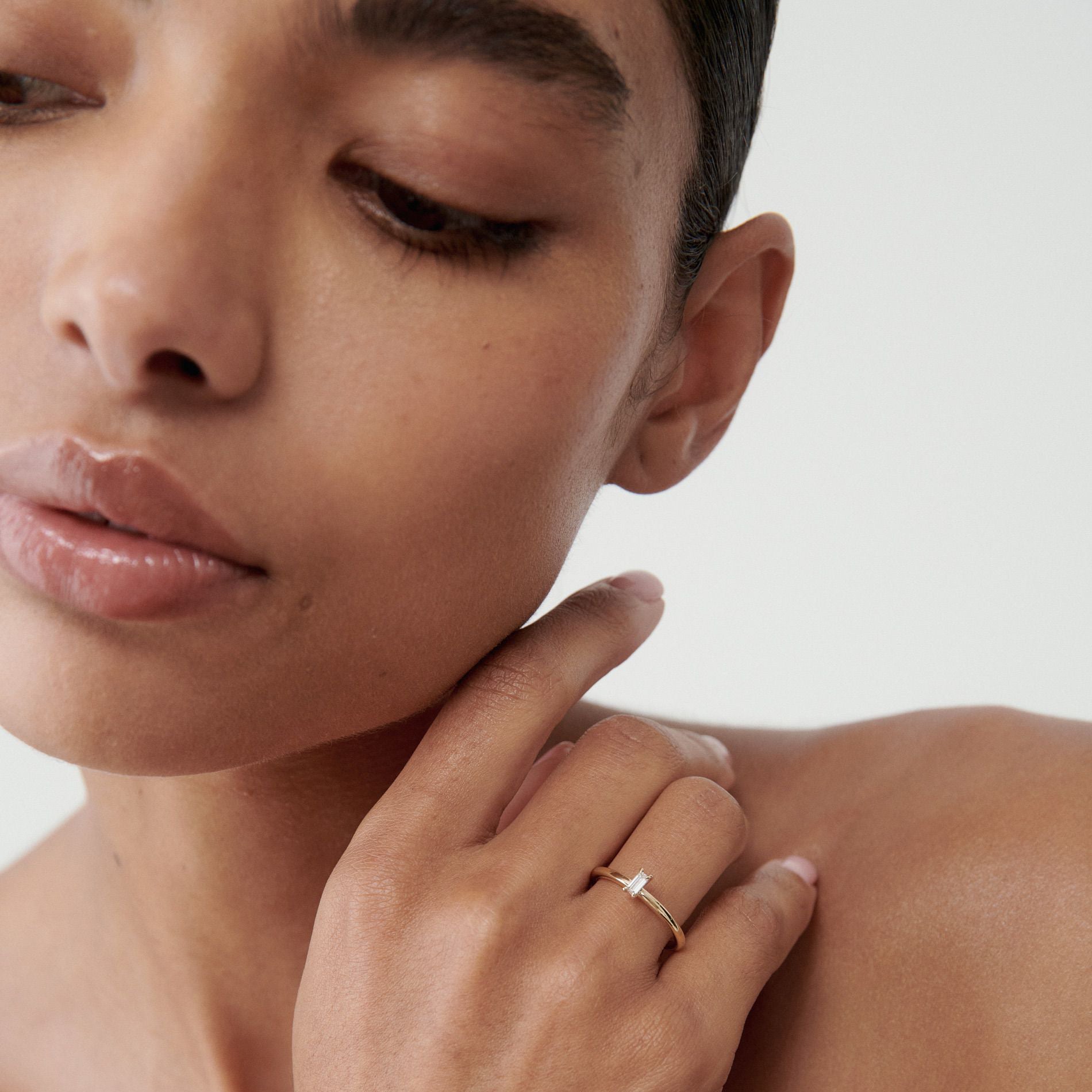 Woman in close-up wearing an elegant gold ring with a diamond. Luxury jewellery. Minimalist style.