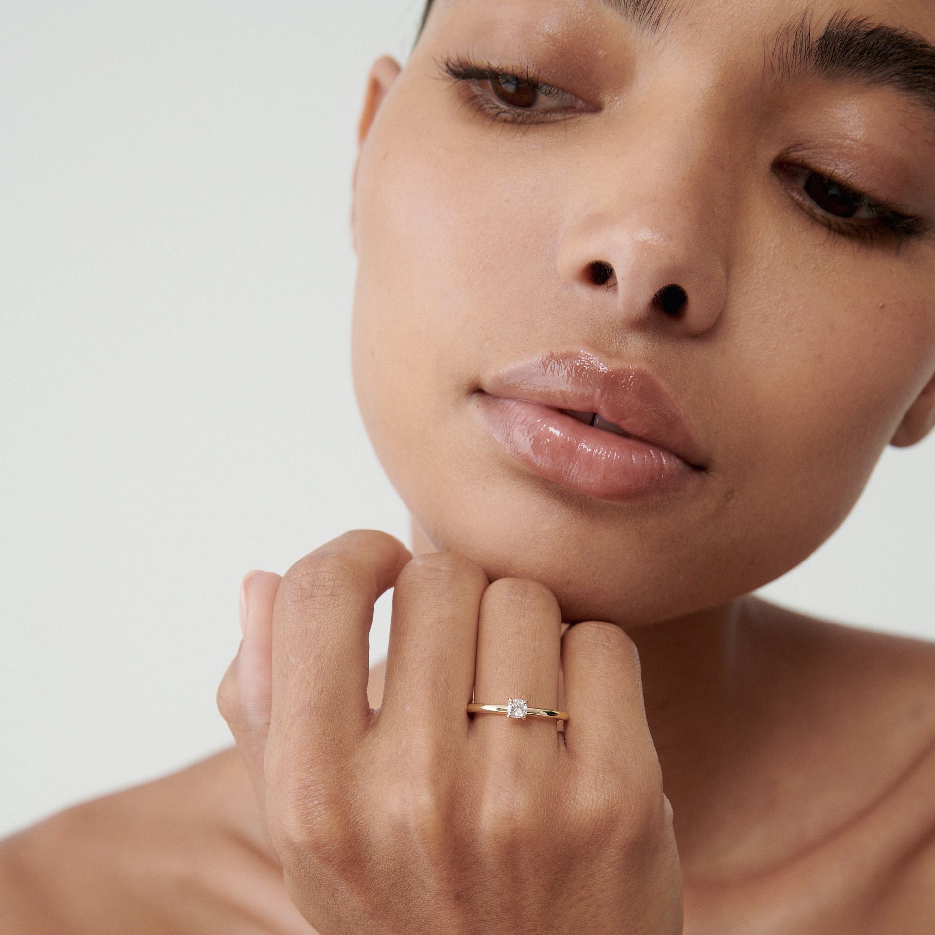 Woman wearing a solitaire diamond ring, touching chin thoughtfully. Close-up of elegant jewellery on hand. Minimalist luxury style.