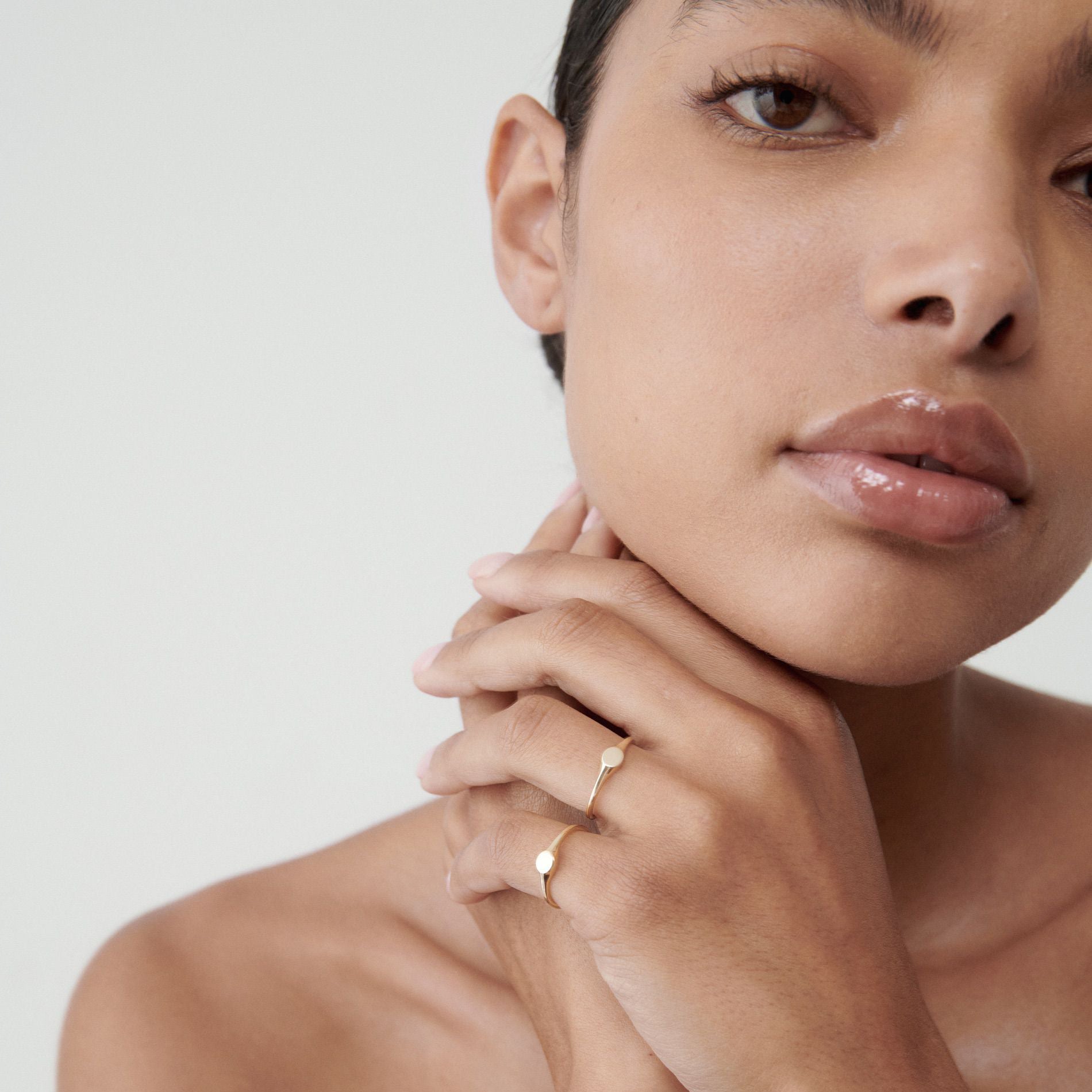Woman with glossy lips and bare shoulders wearing a minimalist gold ring.