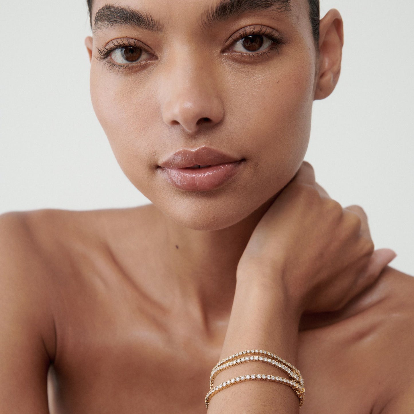 Woman with elegant diamond bracelets on wrist, showcasing luxury jewellery against a neutral background.