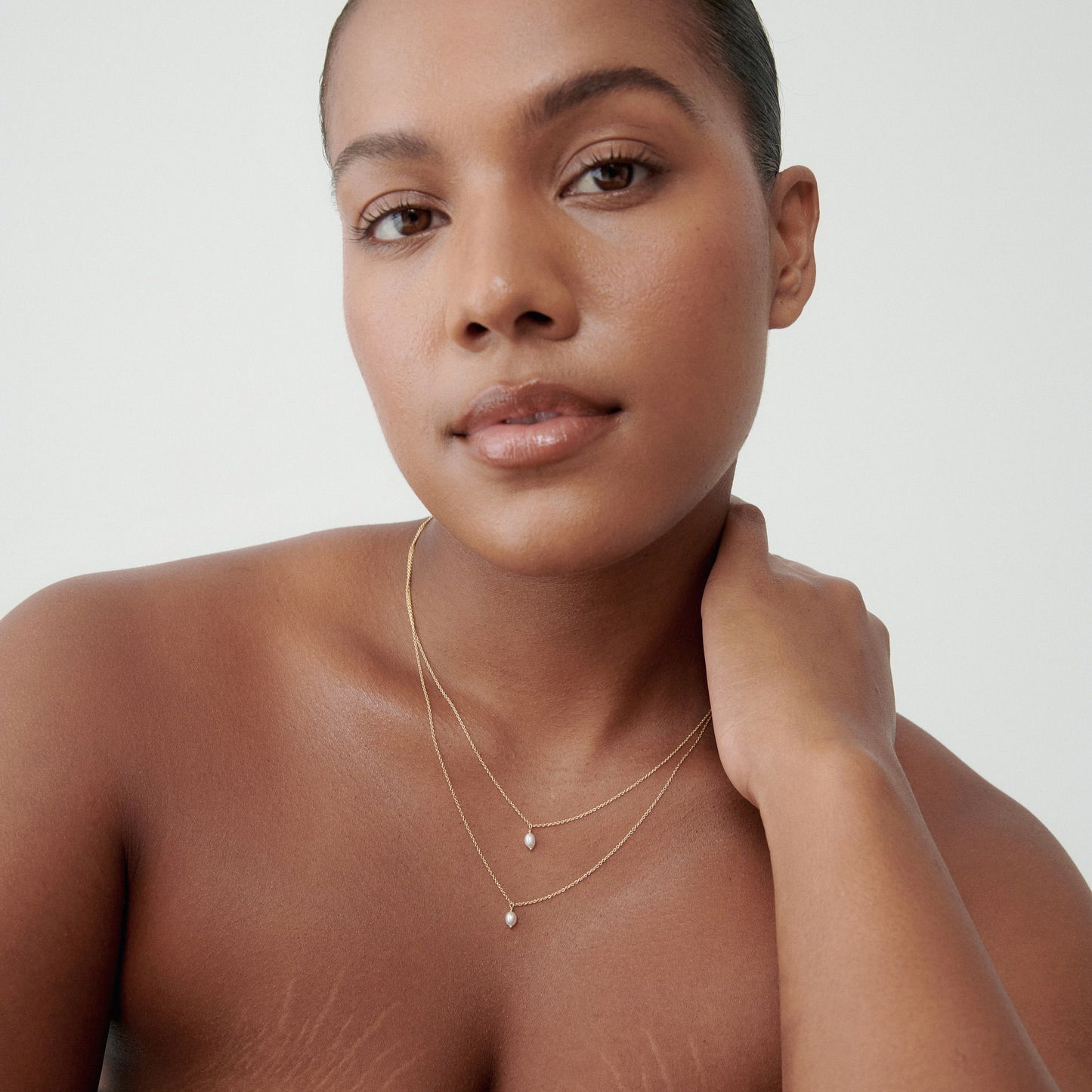 Woman wearing layered gold necklaces with small pearl details, set against a plain background. Elegant jewellery for a luxury look.