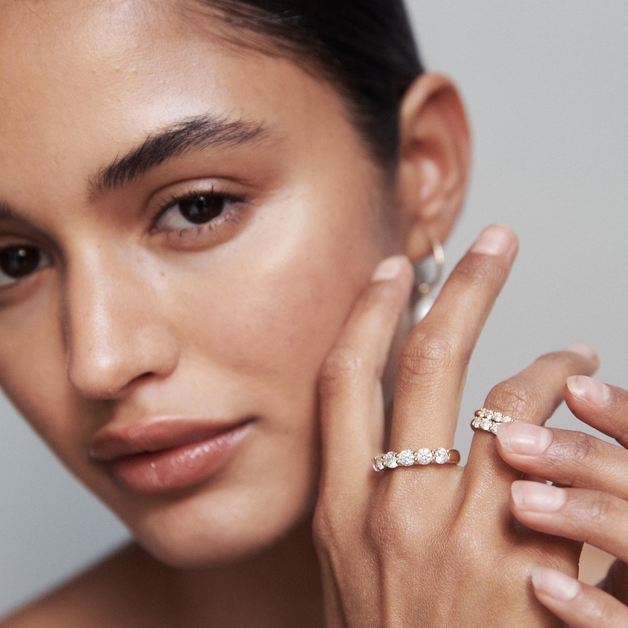 Woman showcasing diamond rings, wearing hoop earrings. Luxury jewellery, close-up of hand and face with elegant style.