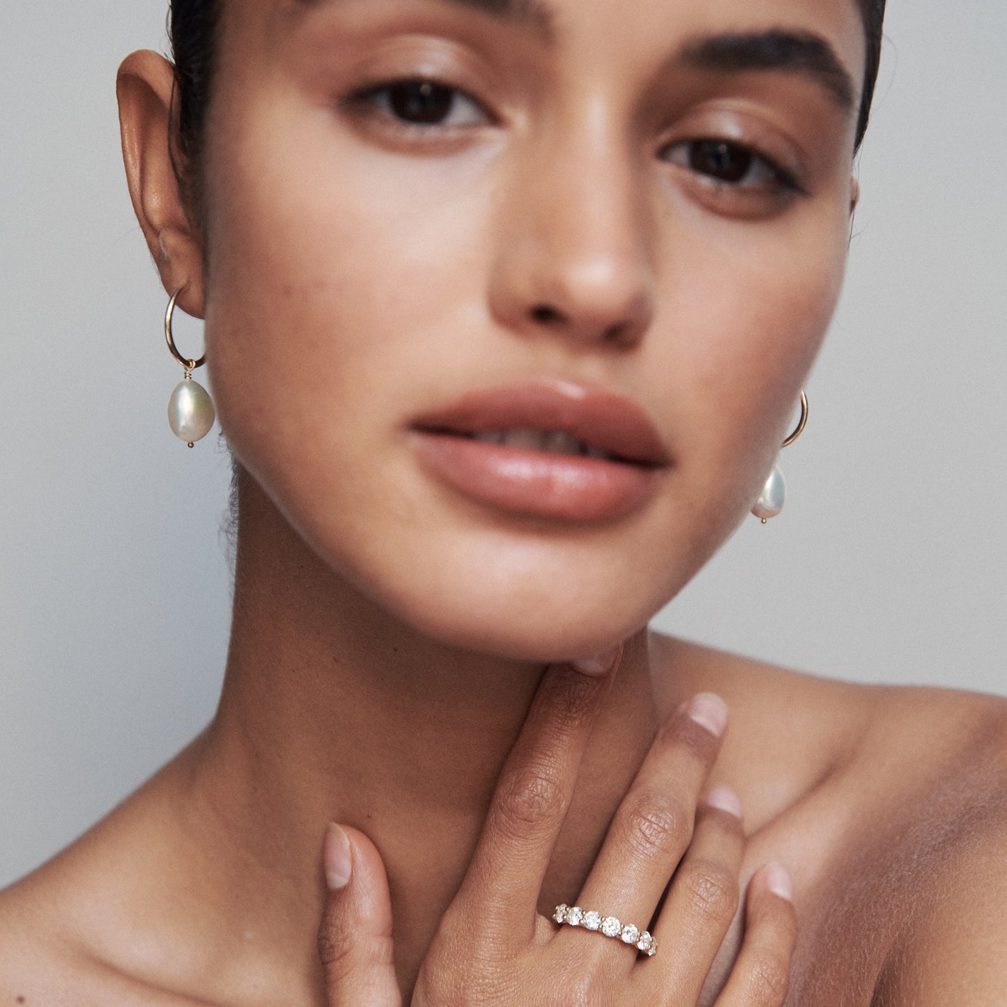 Woman wearing pearl drop earrings and a diamond ring, with a soft-focus effect. Elegant high-end jewellery fashion.
