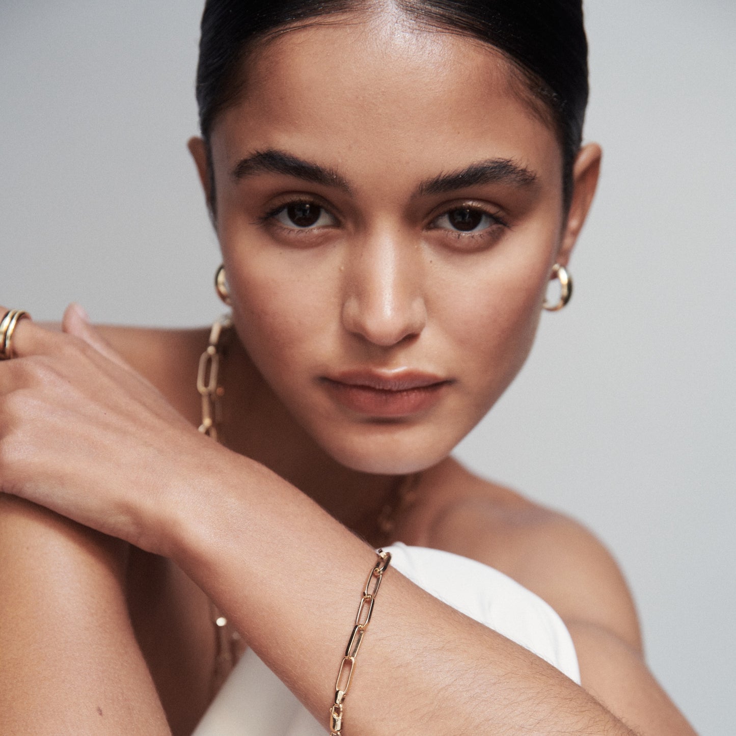 Woman showcasing luxury jewellery: gold hoop earrings, chain necklace, and bracelet. Elegant and high-end aesthetic.