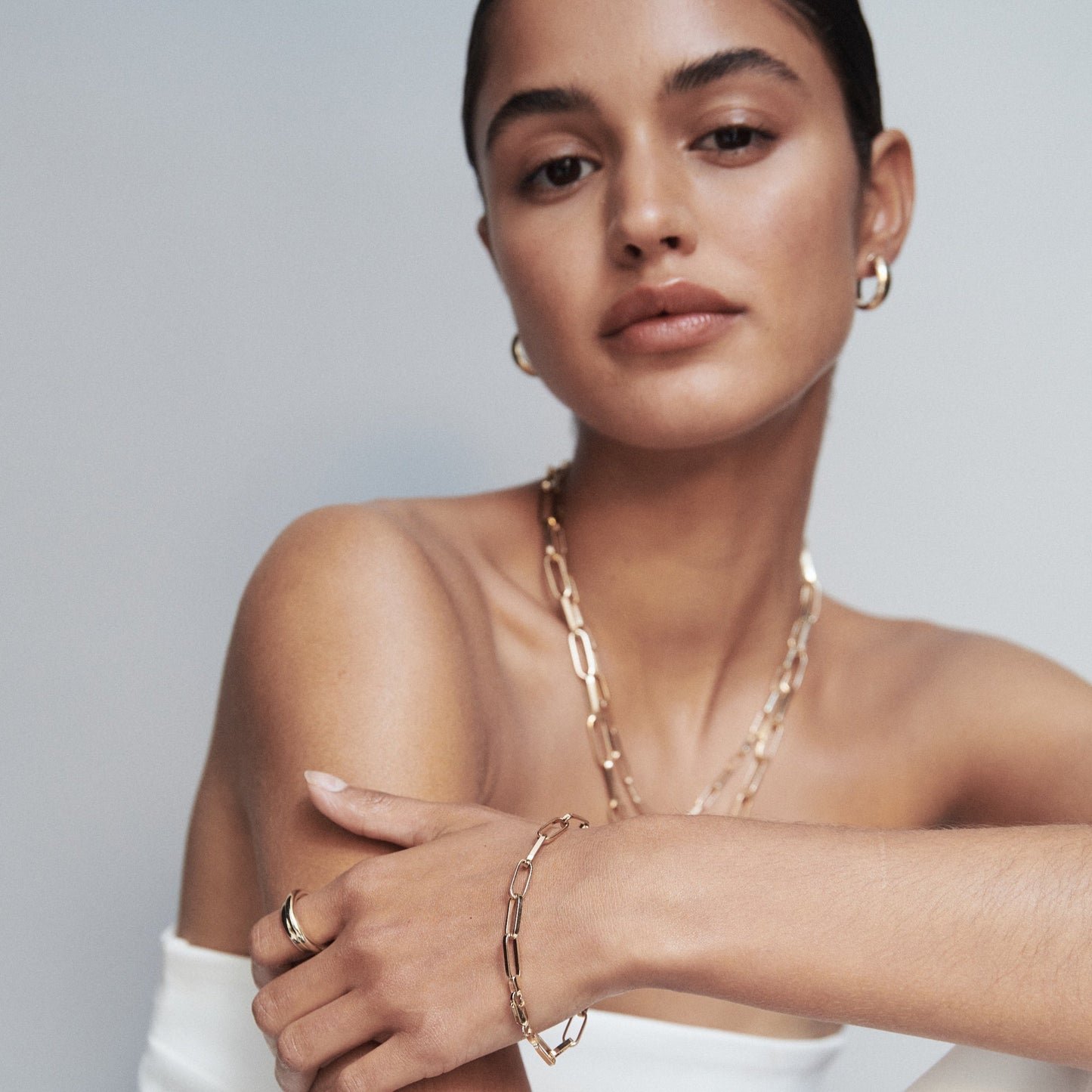 Model wearing gold link bracelet with layered jewellery