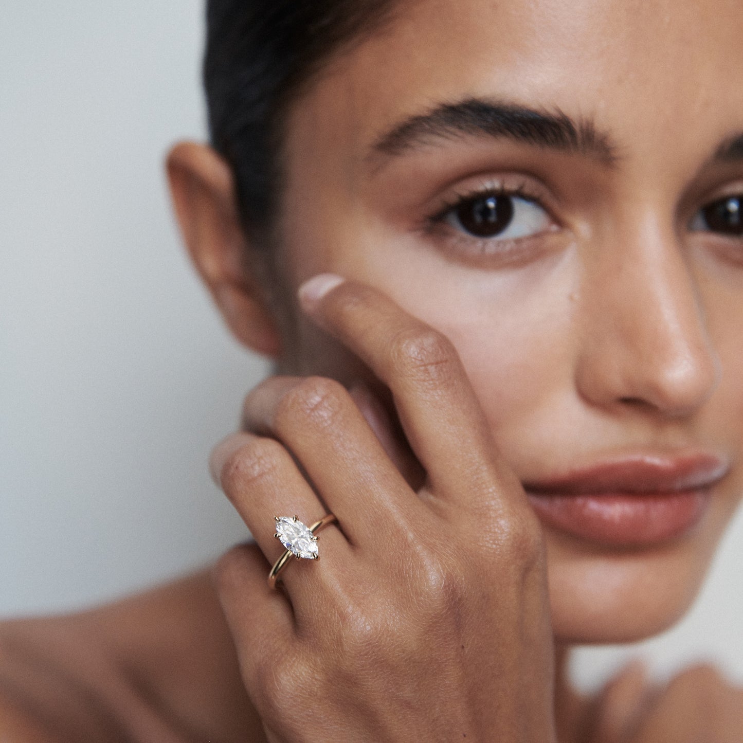 Woman showcasing a marquise-cut diamond ring with a gold band. Luxury jewellery, close-up on hand and face, elegant and refined style.