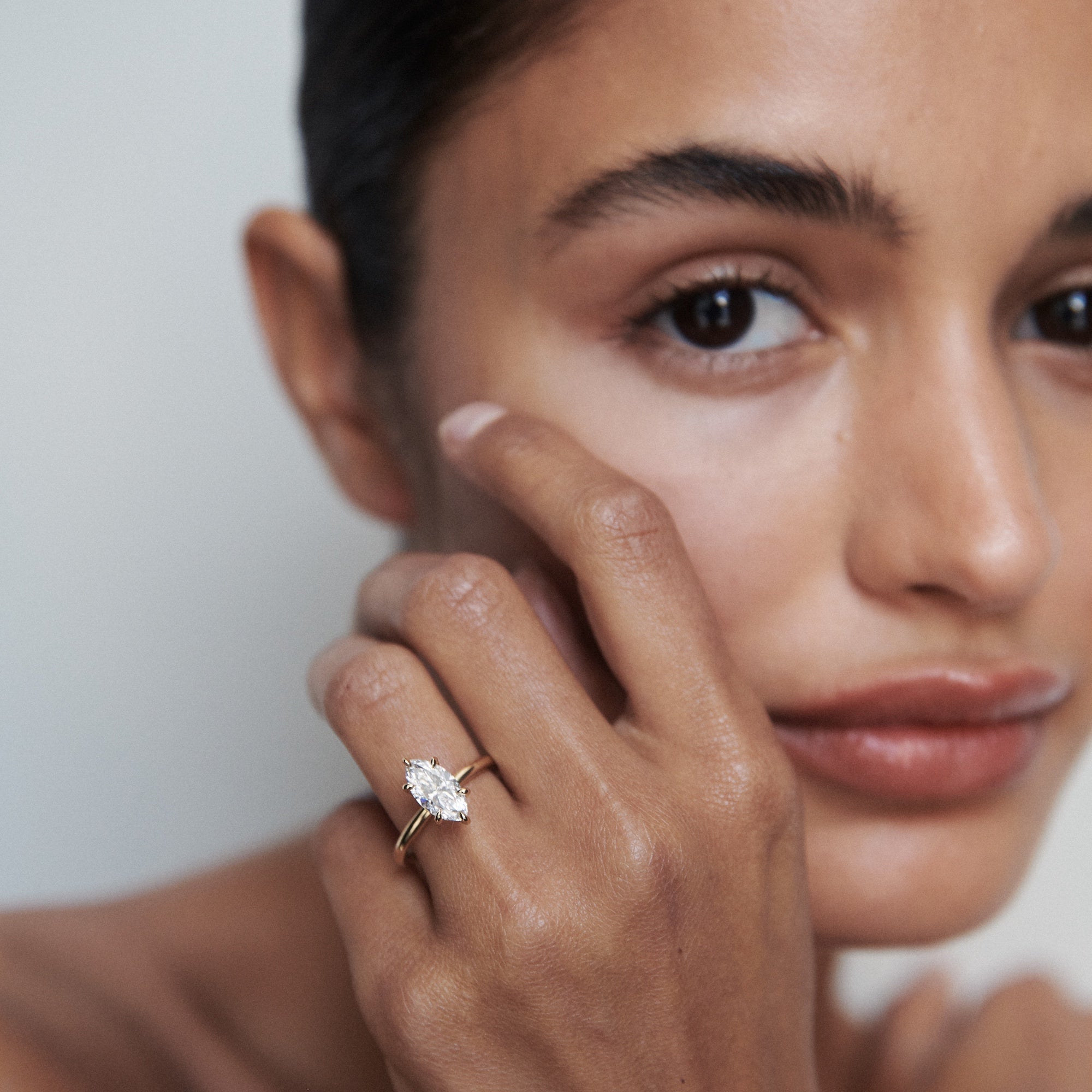 Woman showcasing a marquise-cut diamond ring with a gold band. Luxury jewellery, close-up on hand and face, elegant and refined style.