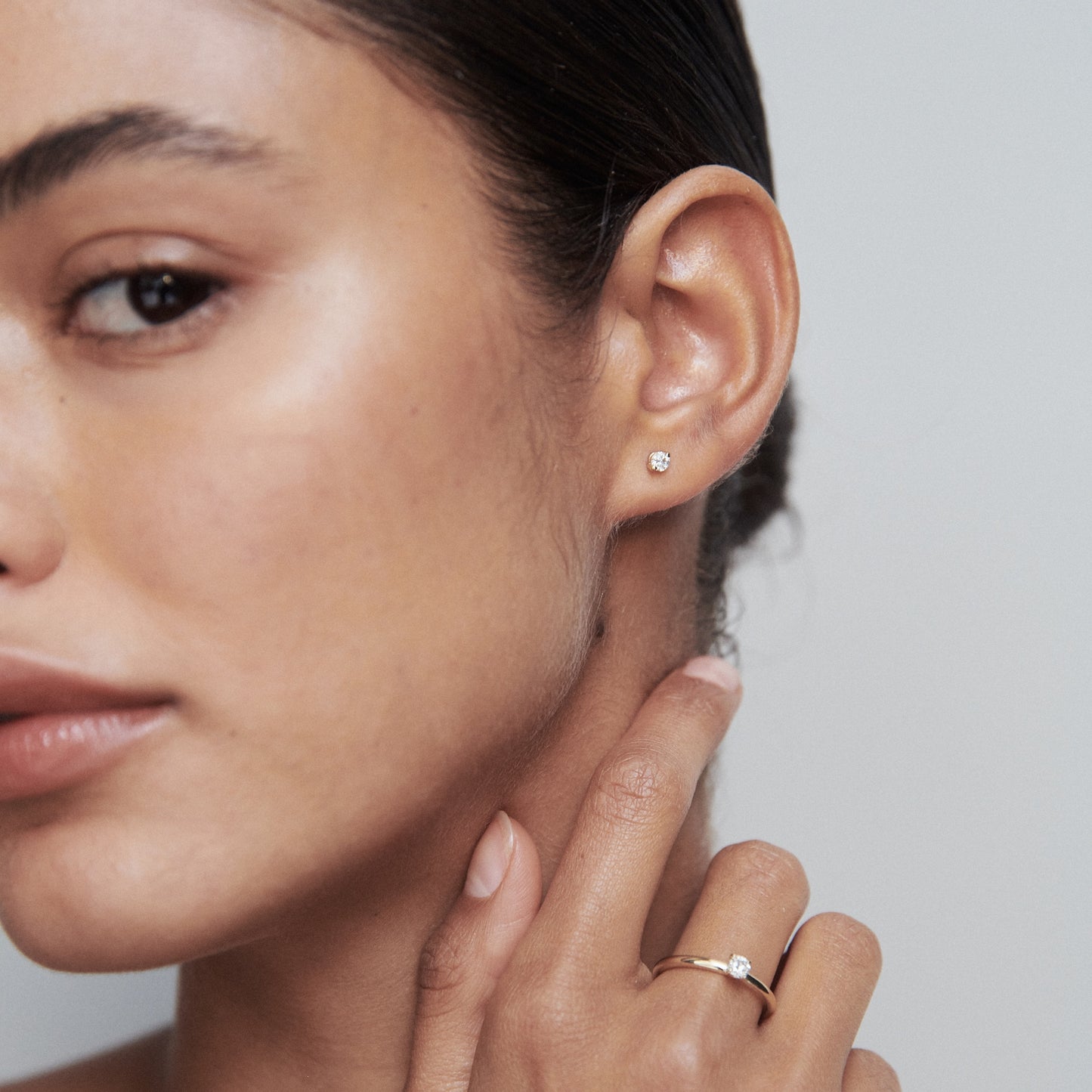 Close-up of a woman wearing a delicate diamond earring and ring, showcasing luxury jewellery in a minimalist style.