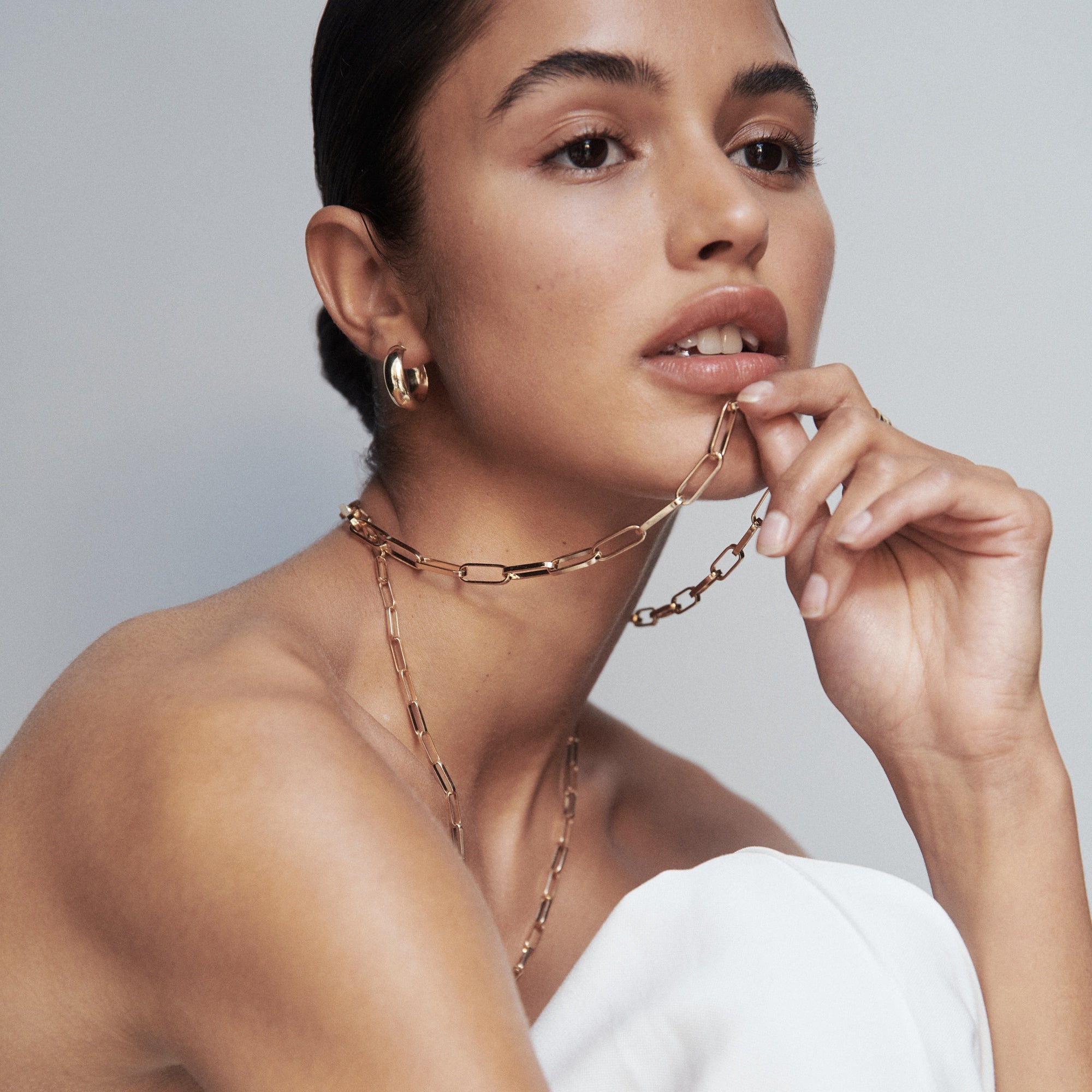 Woman wearing elegant gold chain necklace and hoop earrings, styled with a strapless white top. Luxe jewellery fashion showcasing minimalist elegance.