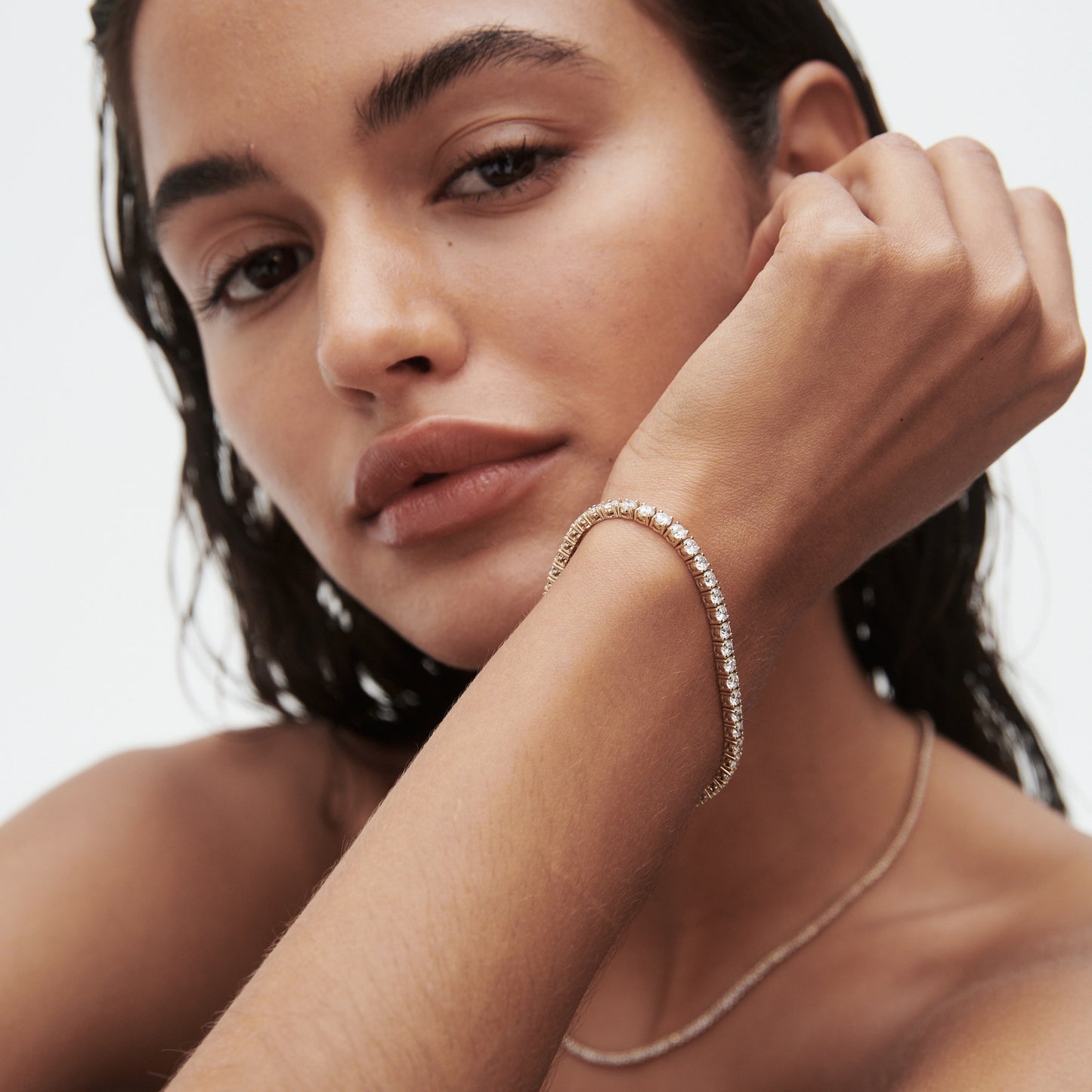 Woman wearing an elegant diamond tennis bracelet, showcasing luxury jewellery. Natural makeup and wet-look hair enhance the sophisticated style.