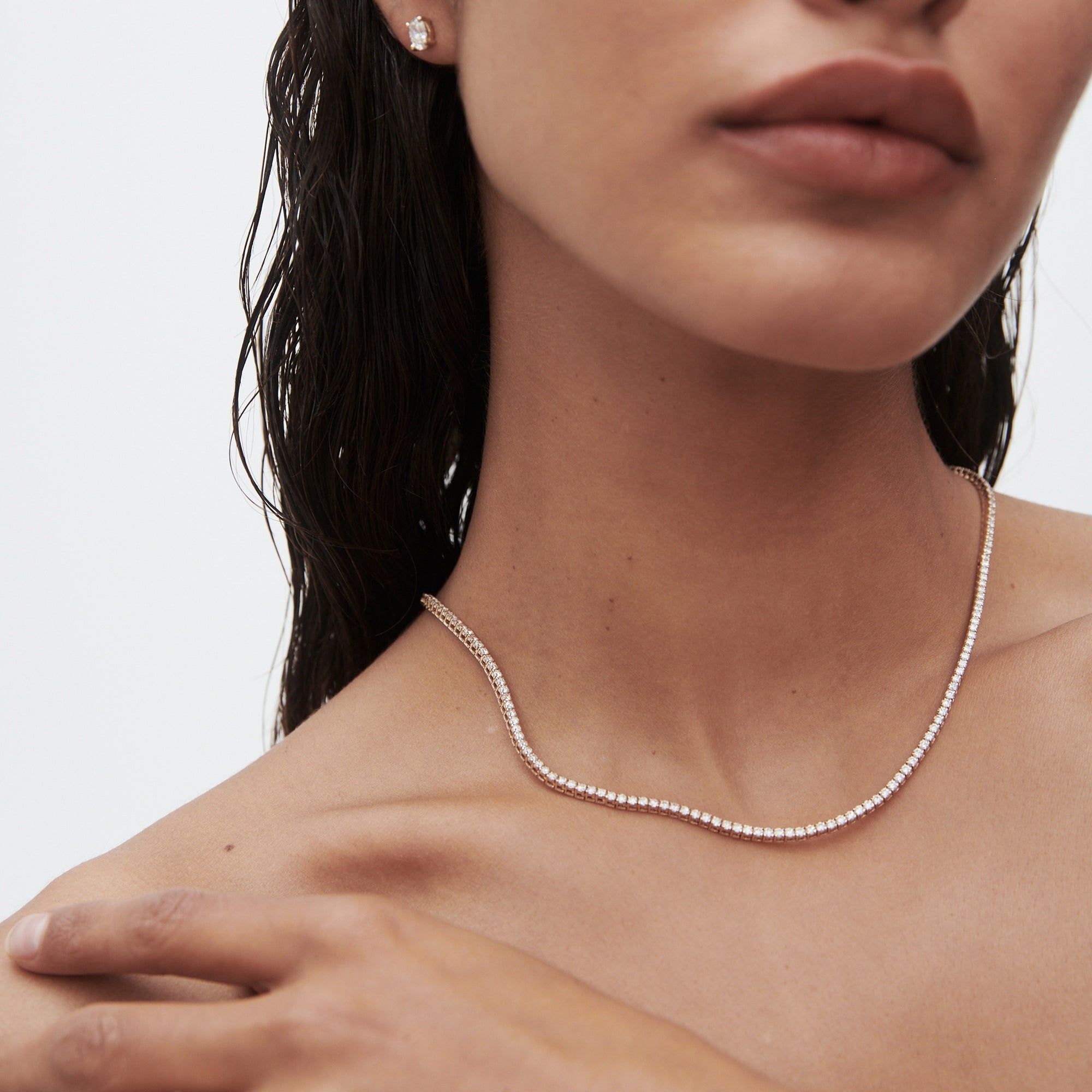Woman wearing an elegant diamond necklace and matching stud earring. She has wet hair, highlighting the luxury jewellery on her skin.