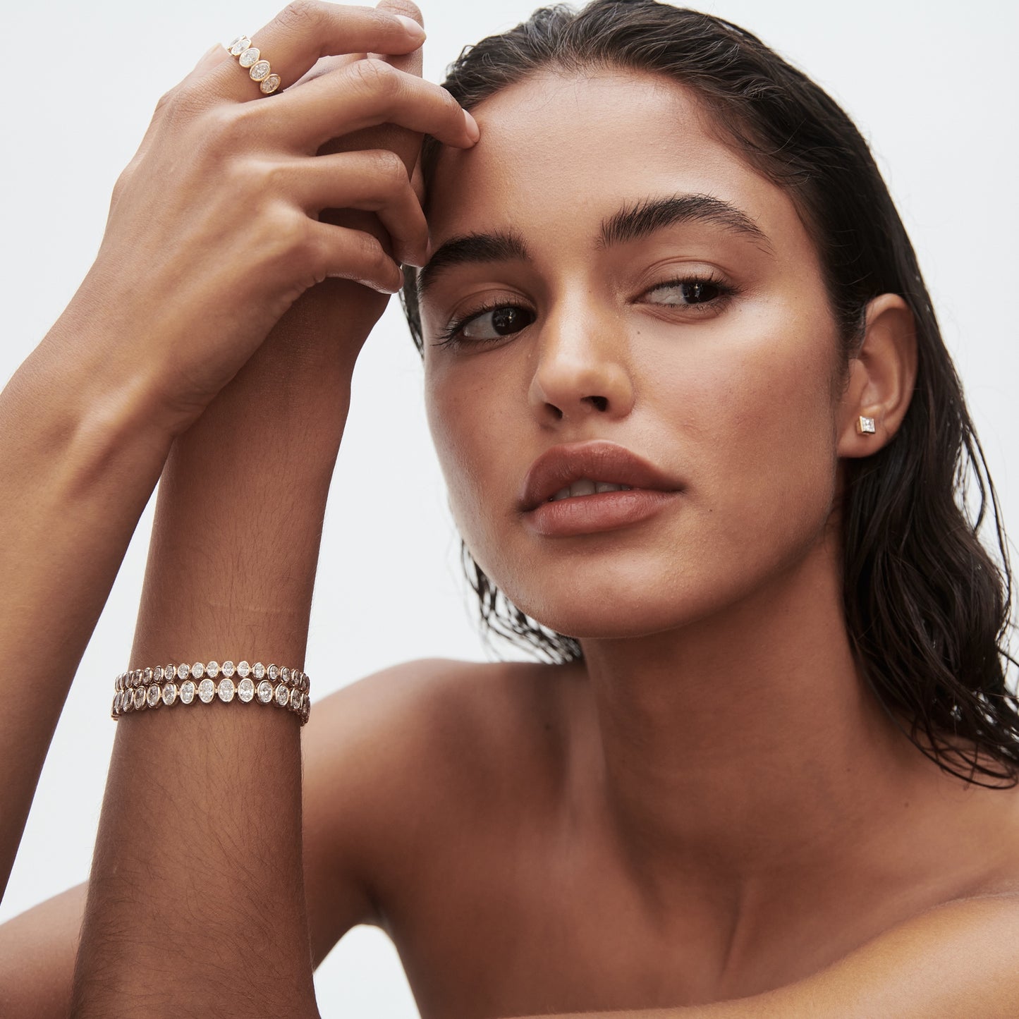 Woman with wet hair wearing a diamond ring, bracelet, and earrings. Elegant jewellery fashion, neutral background.