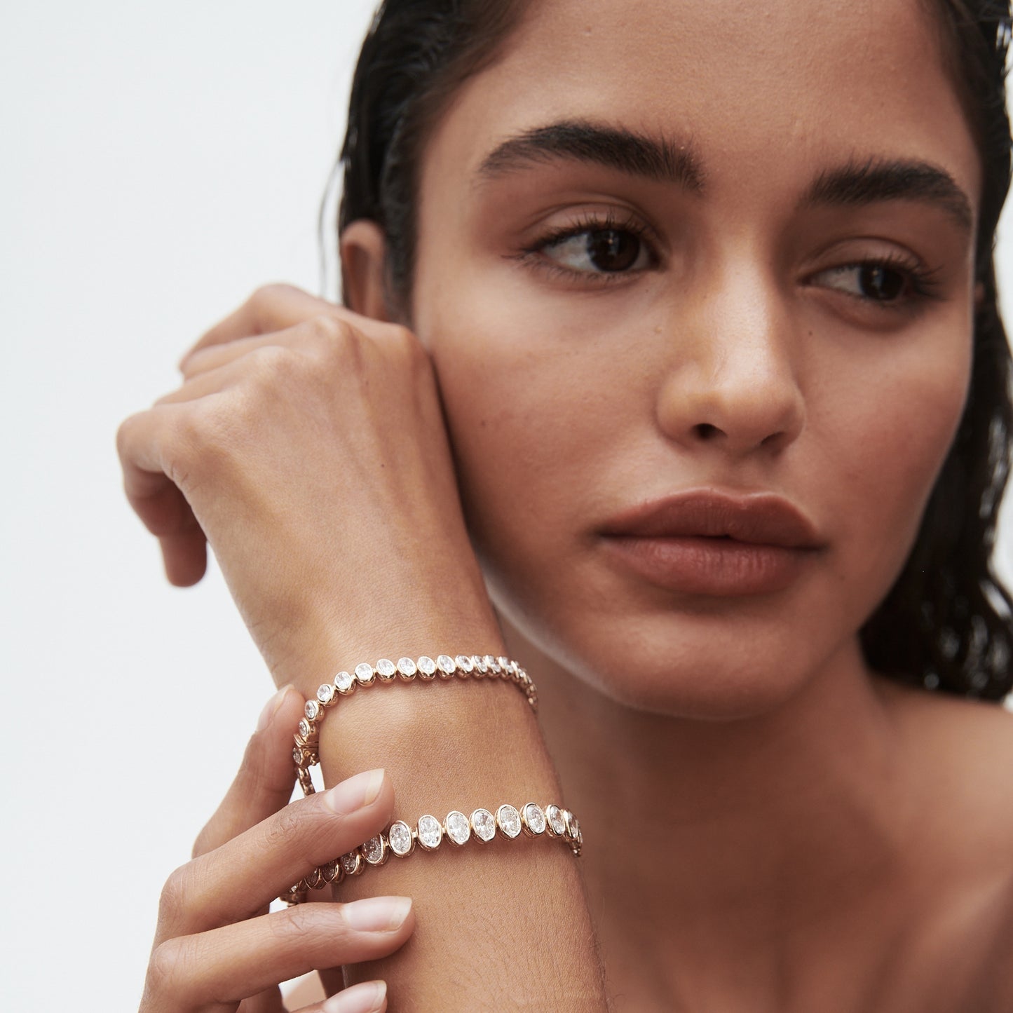 Woman showcasing two elegant gold bracelets adorned with diamonds, highlighting luxury jewellery. Minimalist, high-end aesthetic.