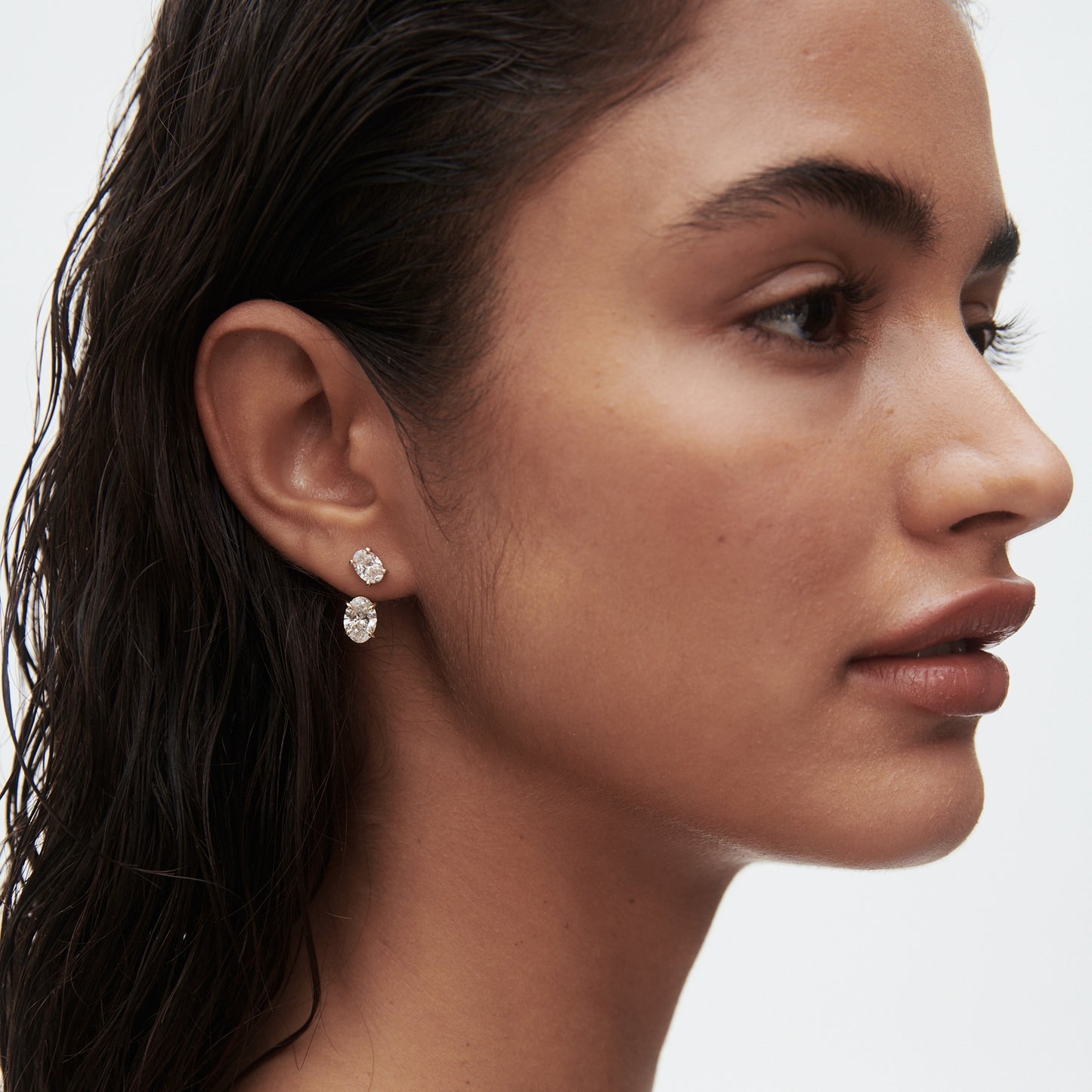 Woman with wet hair wearing two luxury diamond earrings. Her profile view highlights elegant jewellery, emphasising luxury style and sophistication.