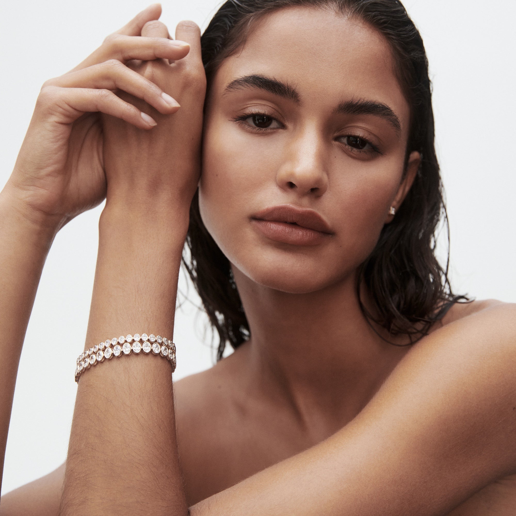 Woman with wet hair and minimal makeup poses wearing a luxurious diamond bracelet and matching earrings, showcasing elegant jewellery design.