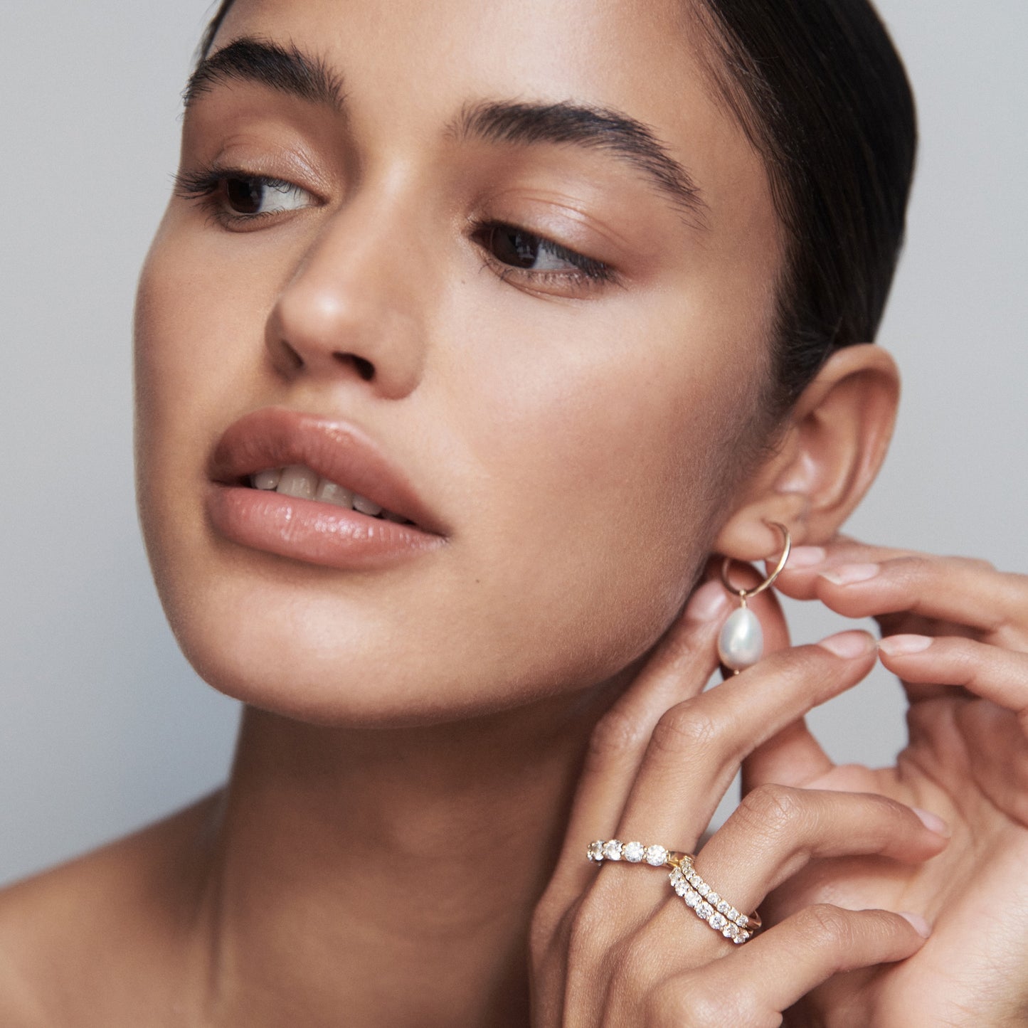 Woman wearing gold hoop earrings with a dangling pearl and a gold diamond ring; showcasing luxury jewellery.