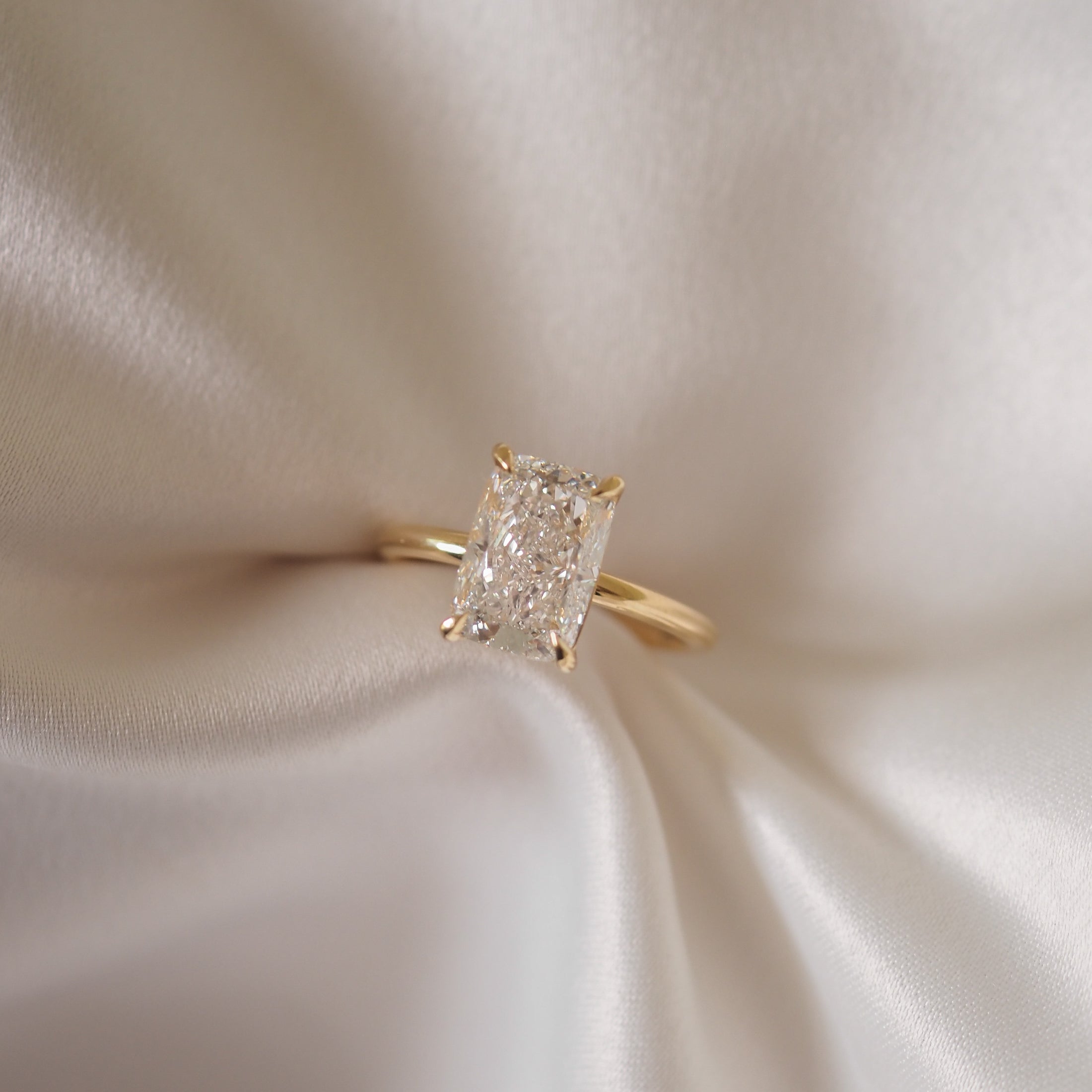 Gold ring with a radiant-cut diamond resting on ivory silk fabric, showcasing luxury jewellery design.