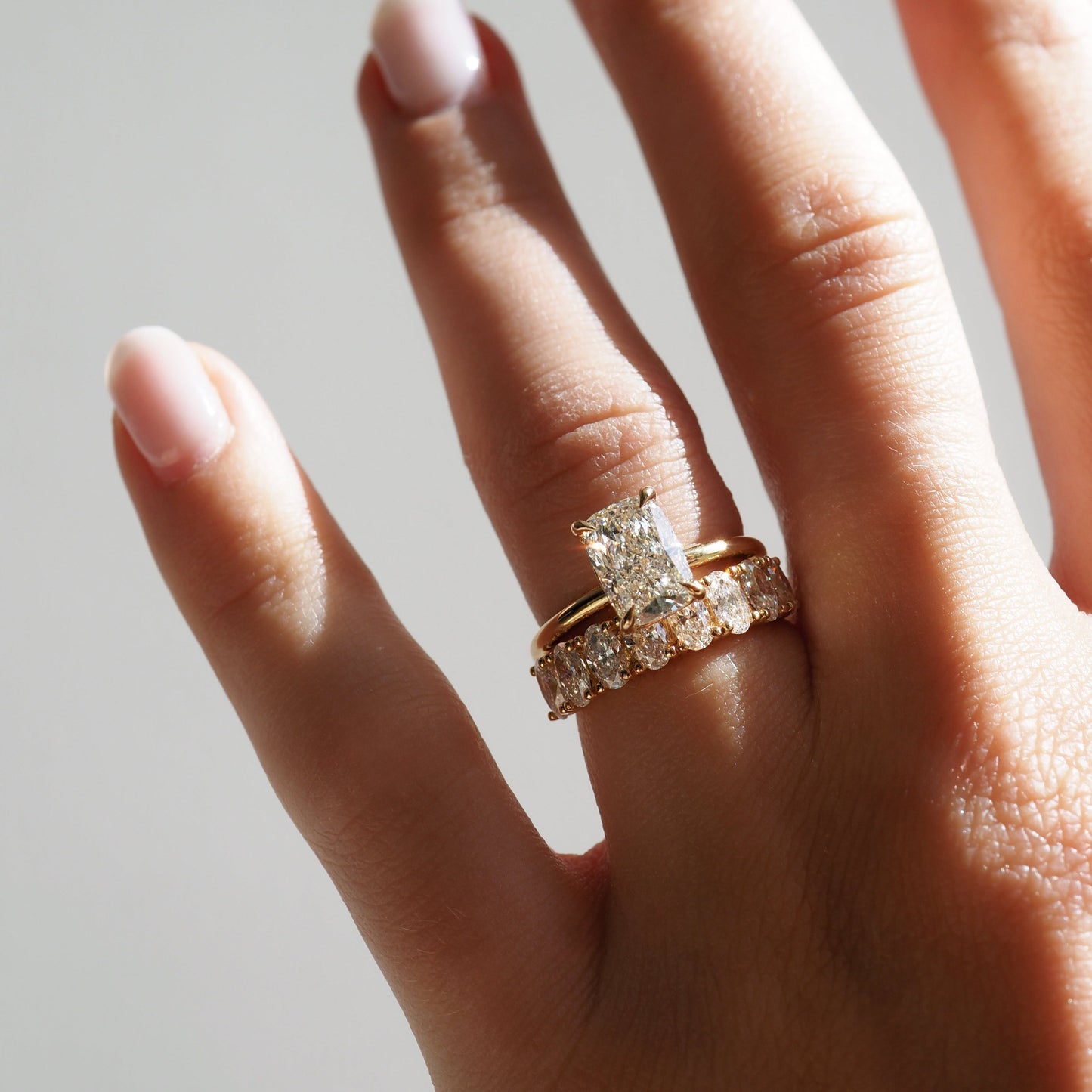 Close-up of a hand wearing two gold rings with radiant-cut diamonds, showcasing luxury jewellery against a soft, natural light background.