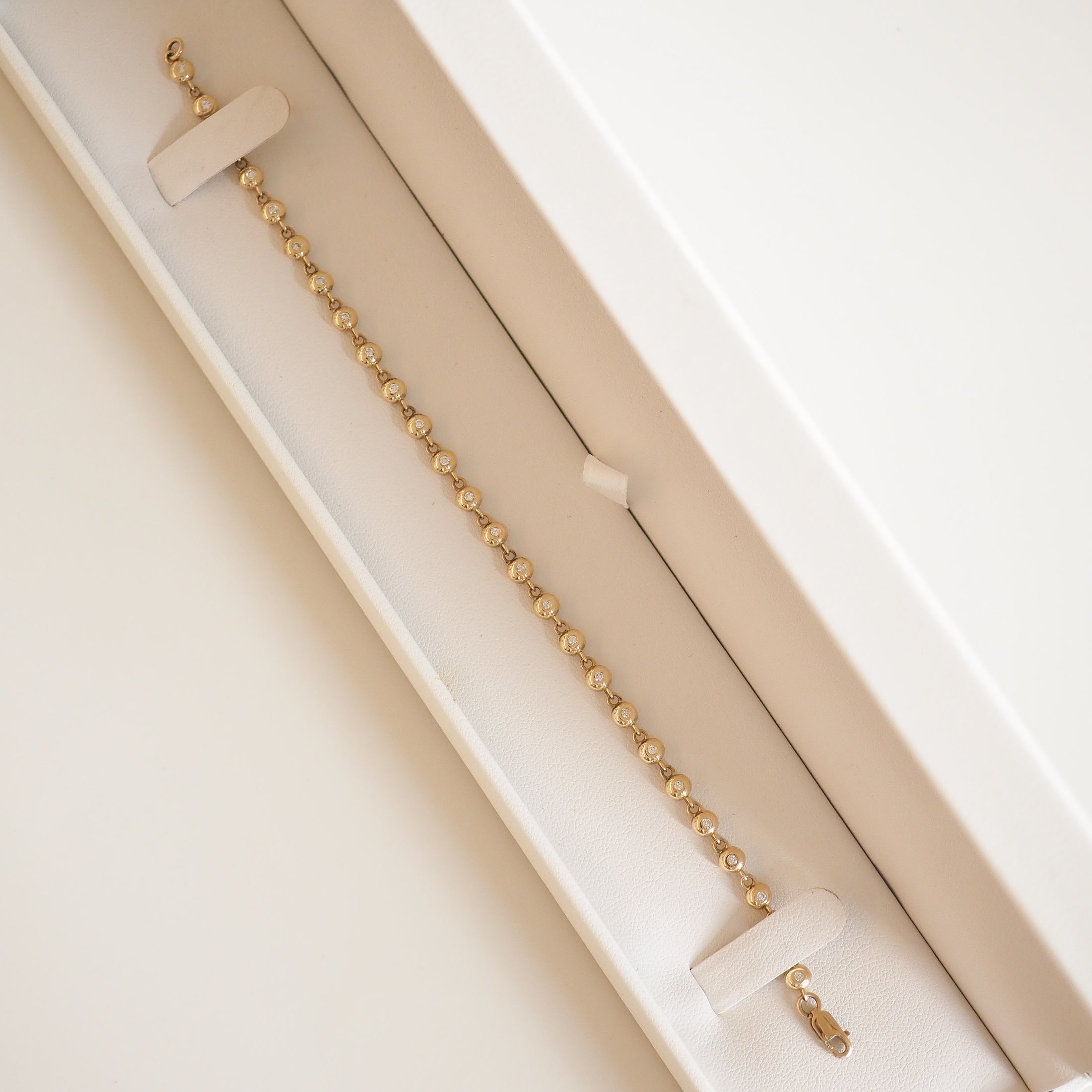 Gold bead bracelet in an elegant cream jewellery box, displayed diagonally. Ideal for luxury jewellery enthusiasts.