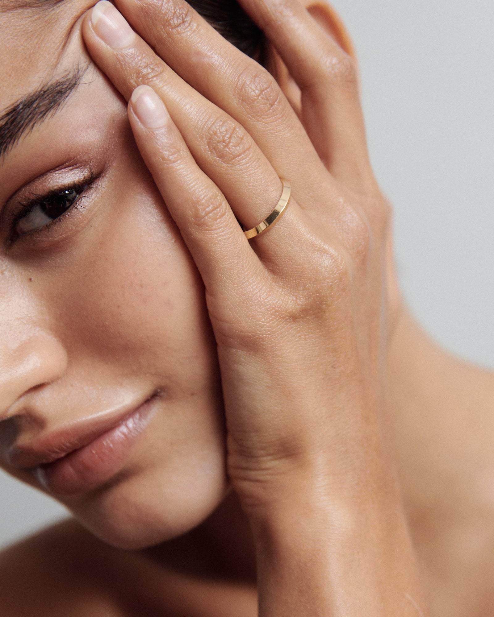 Woman with knife edge band on hand on face against a neutral background