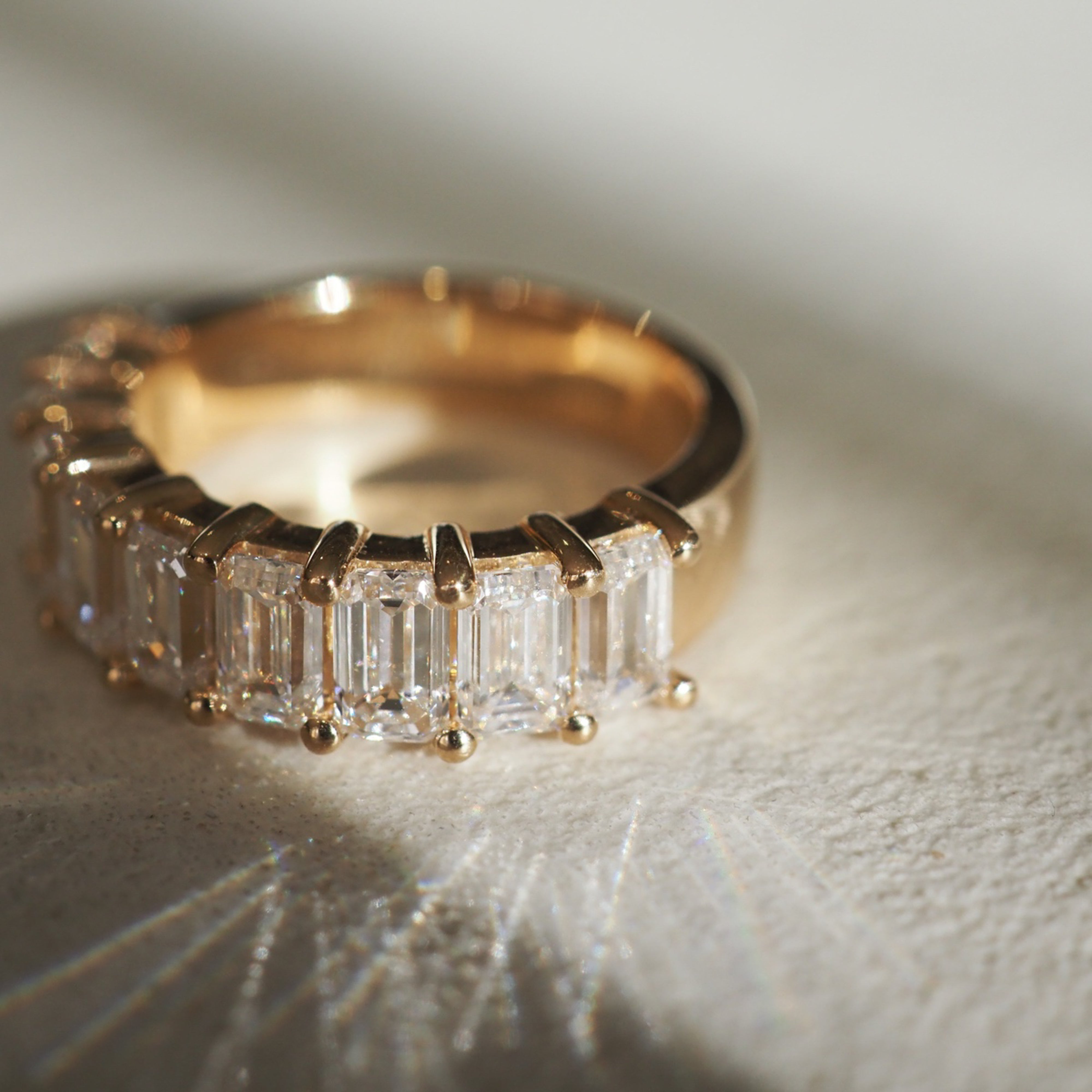 Gold ring with rectangular cut diamonds on a textured surface, catching light reflections. Luxury jewellery in an elegant setting.