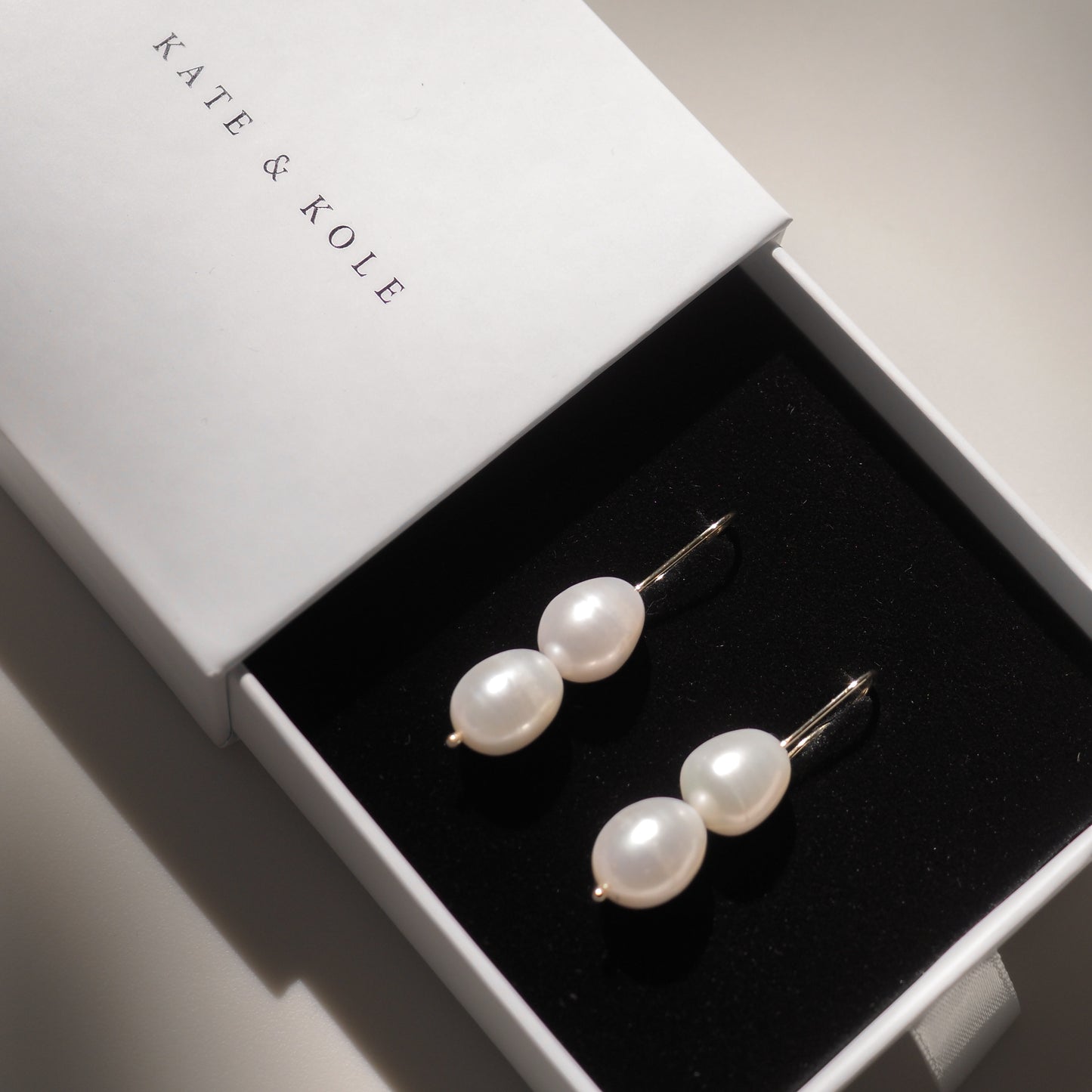 Elegant pair of pearl drop earrings in a Kate & Kole jewellery box, featuring a minimalist design with a luxurious touch.