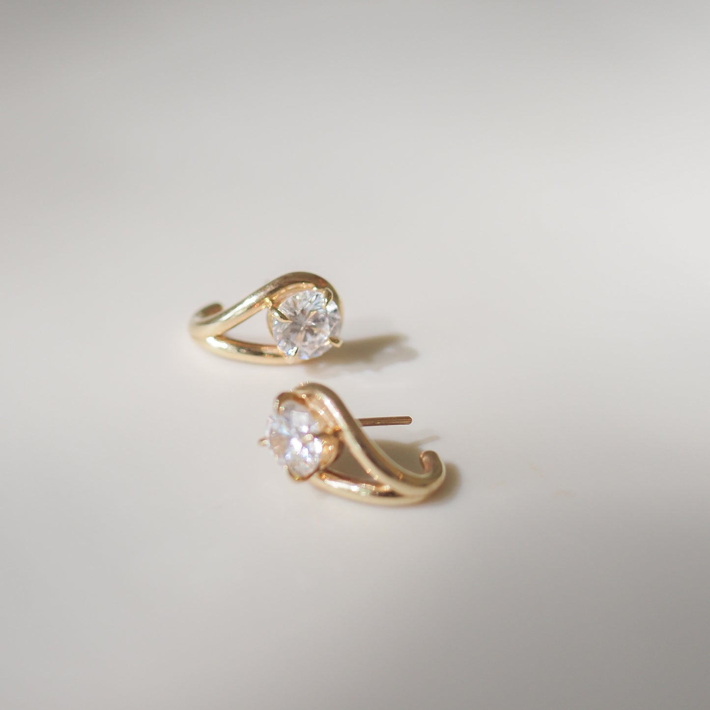 Elegant gold earrings featuring sparkling round diamonds in a unique twisted design. Luxurious high-end jewellery on a soft background.