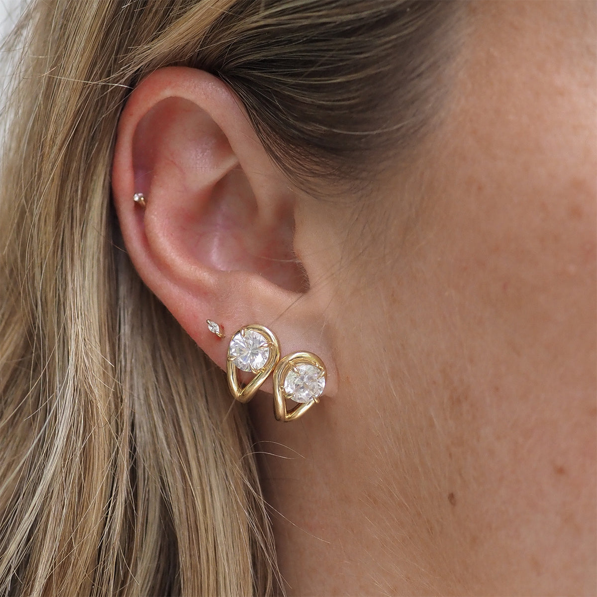 Close-up of a woman's ear adorned with elegant teardrop-shaped gold earrings featuring sparkling gemstones, paired with a small stud.