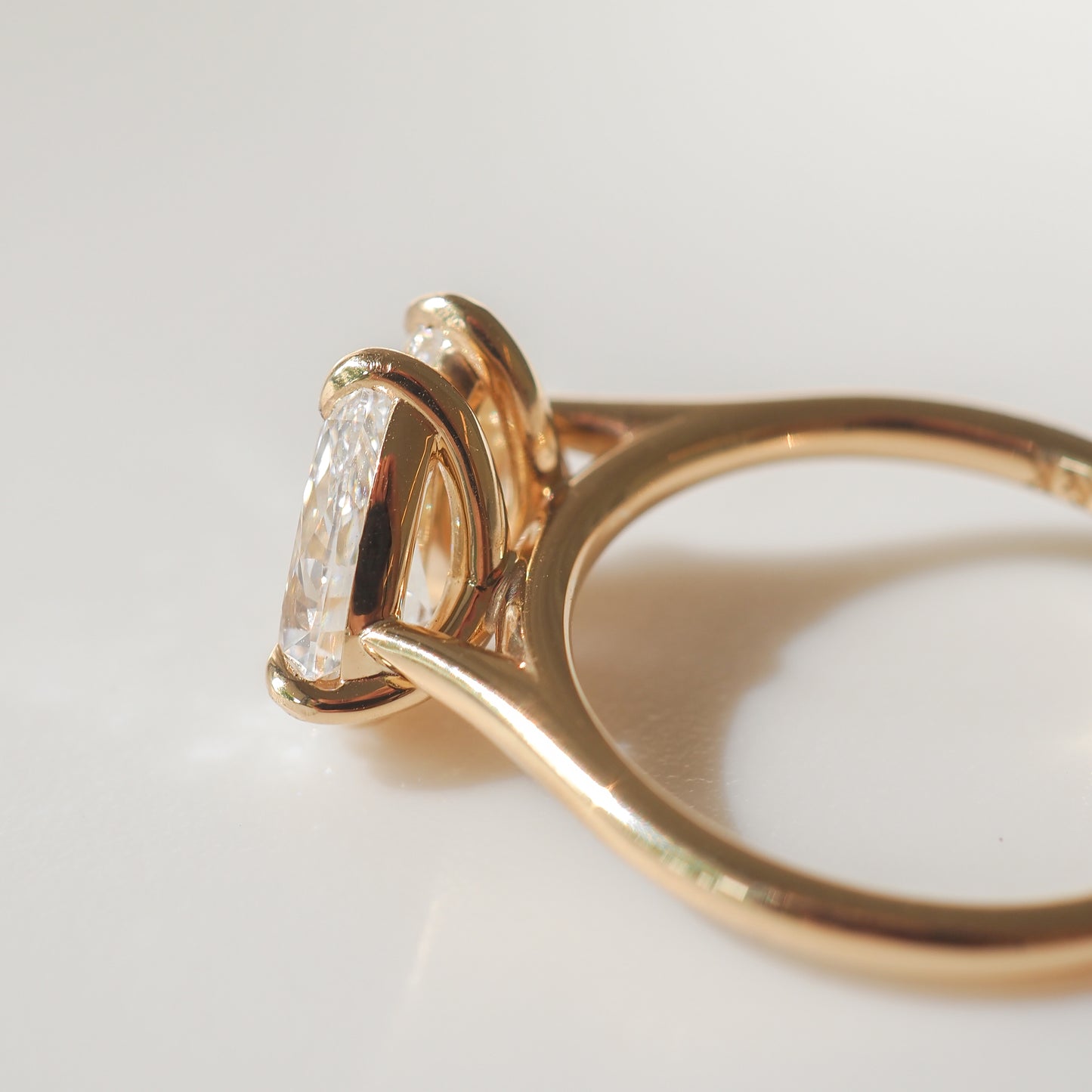 Gold engagement ring with an oval-cut diamond in a prong setting, reflecting light on a smooth surface. Ideal for luxury jewellery lovers.