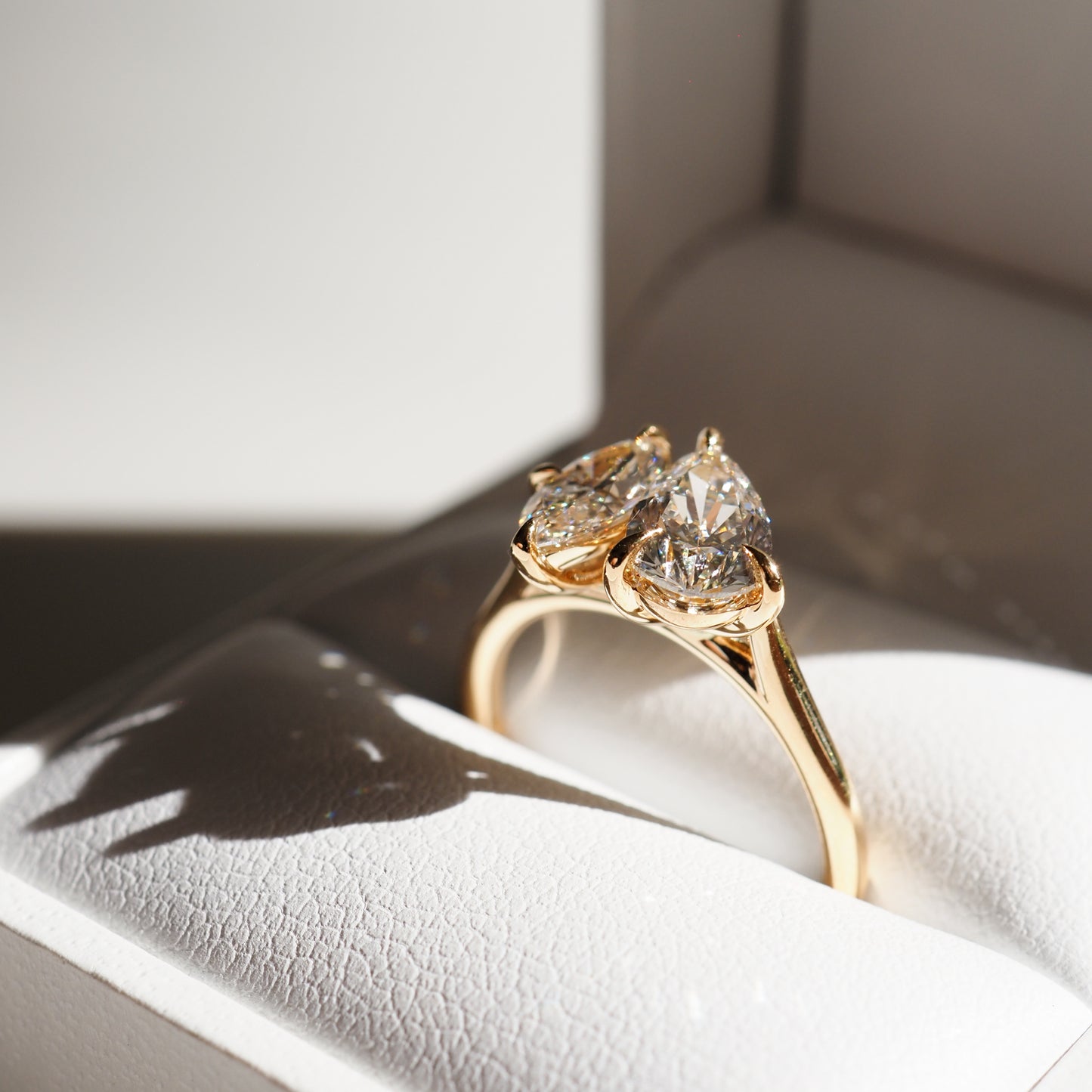 Gold ring with two pear-cut diamonds in a white jewellery box, showcasing luxury craftsmanship and elegance.