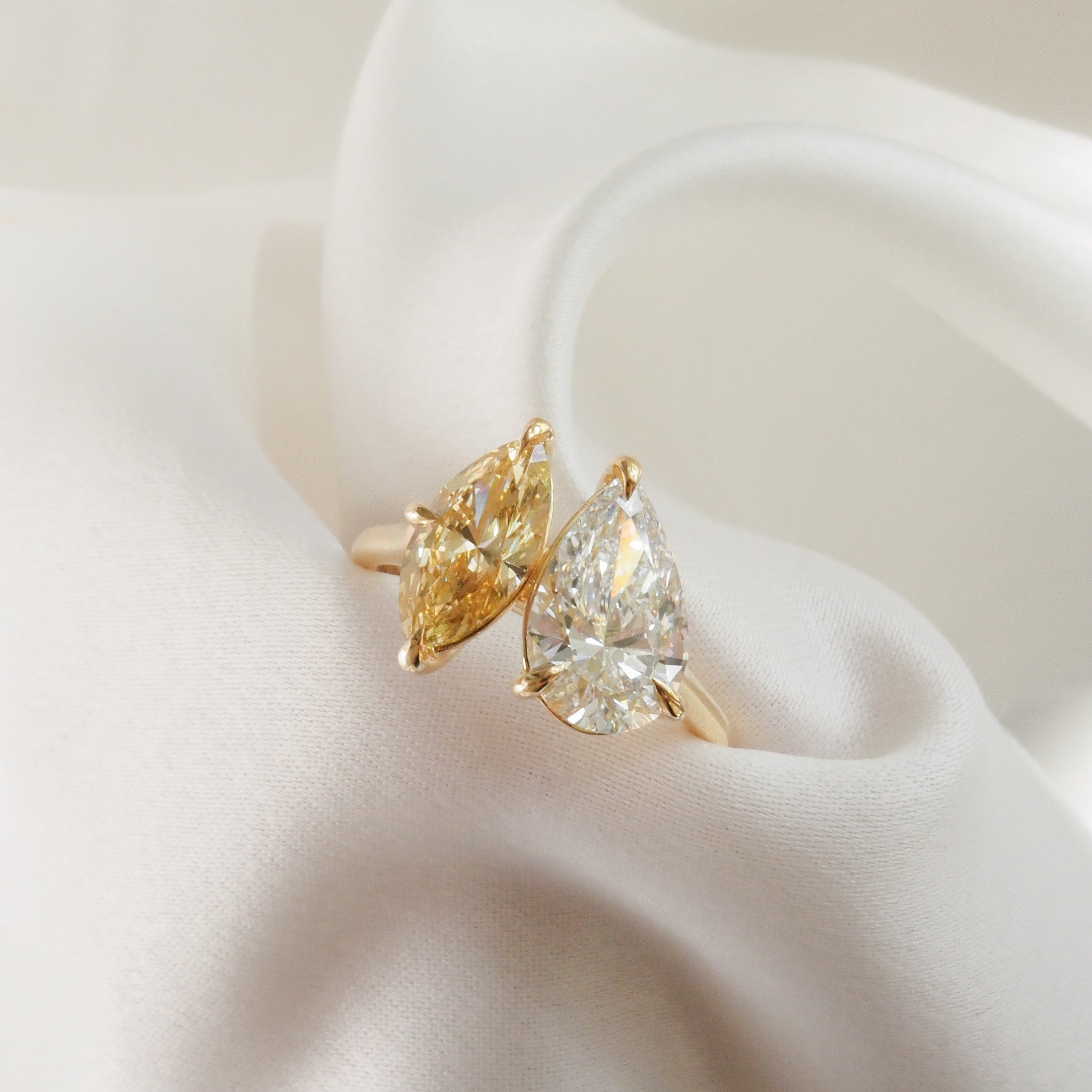 Two pear-cut diamond rings in gold settings, elegantly placed on soft white fabric, showcasing luxury jewellery design.