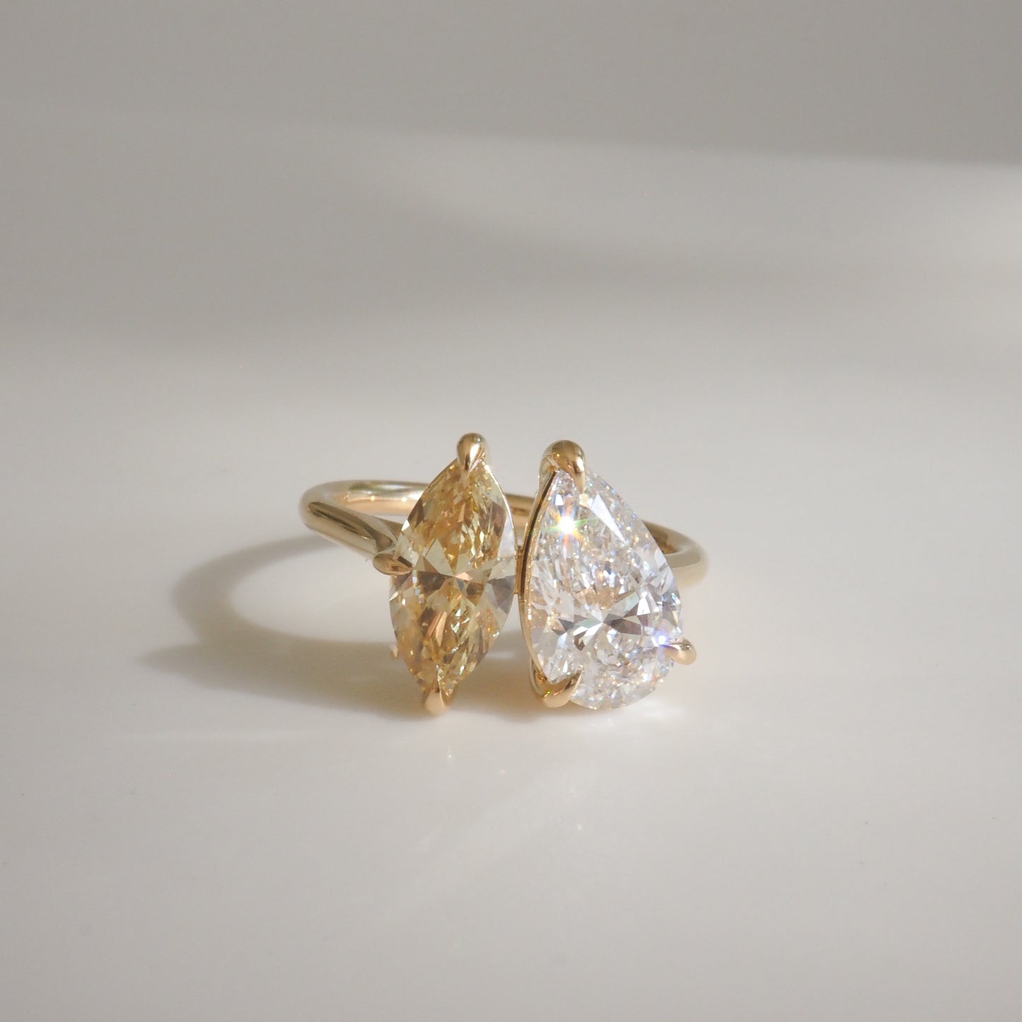 Two-stone diamond ring featuring a pear-cut and a marquise-cut gem set in a gold band, elegantly displayed on a light background.