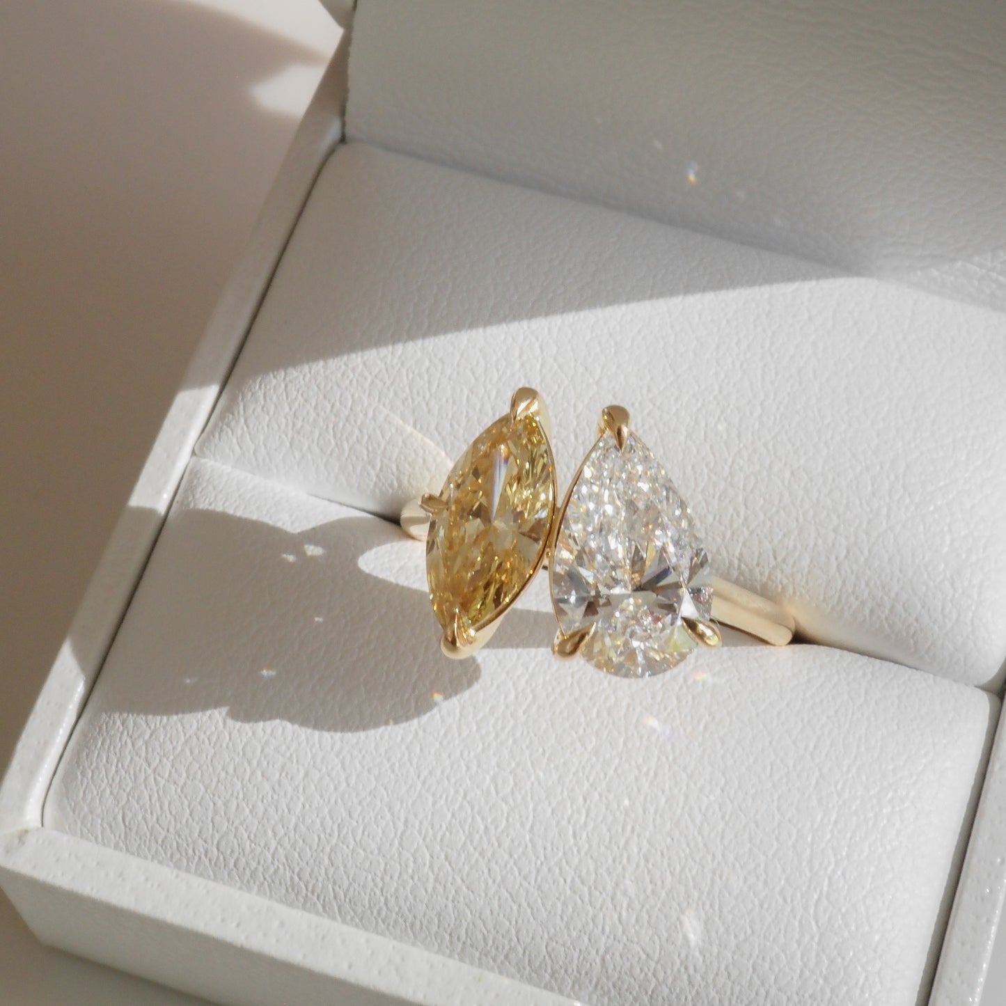 Yellow and clear pear-shaped diamonds set in a gold ring, displayed in an open white jewellery box, showcasing luxury craftsmanship.