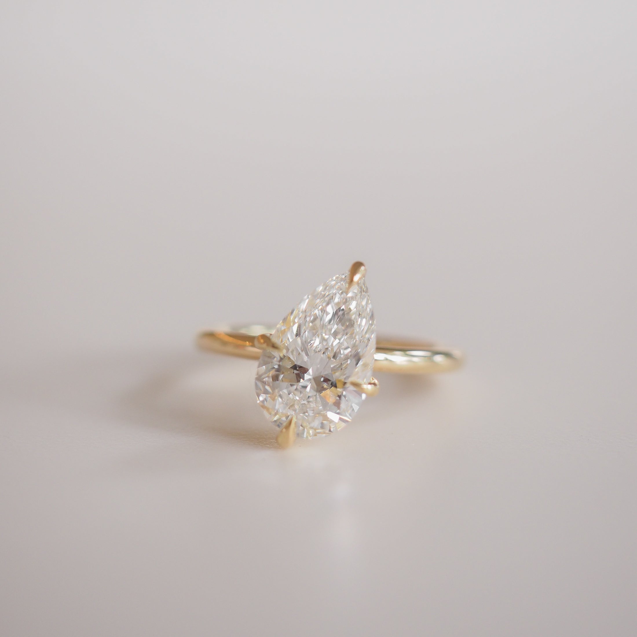 Gold ring with a pear-shaped diamond set in a minimalist prong setting, reflecting luxury and elegance on a light background.