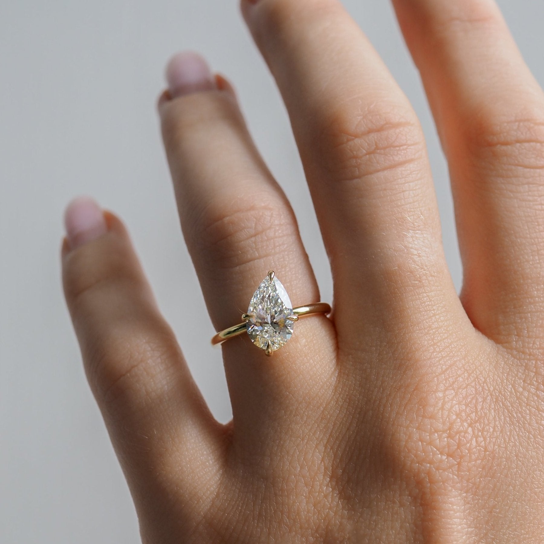 A gold ring with a pear-shaped diamond rests elegantly on a hand with manicured nails, showcasing luxury jewellery design.
