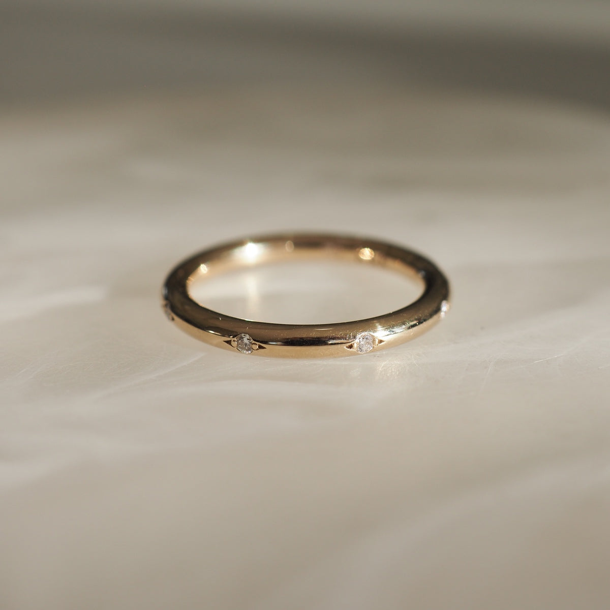 Gold band ring with tiny diamond accents, elegantly displayed on a light marble surface, showcasing luxury jewellery craftsmanship.