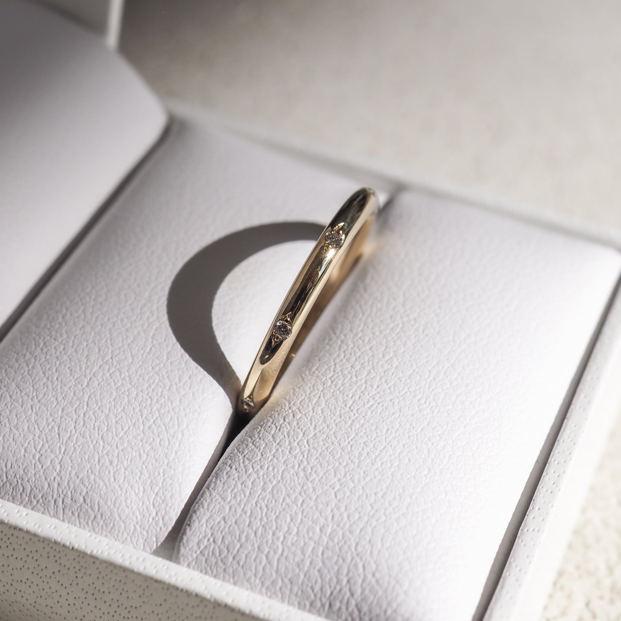 Gold ring with small diamonds in a white jewellery box, casting a shadow. Elegant and luxurious design, ideal for weddings or anniversaries.