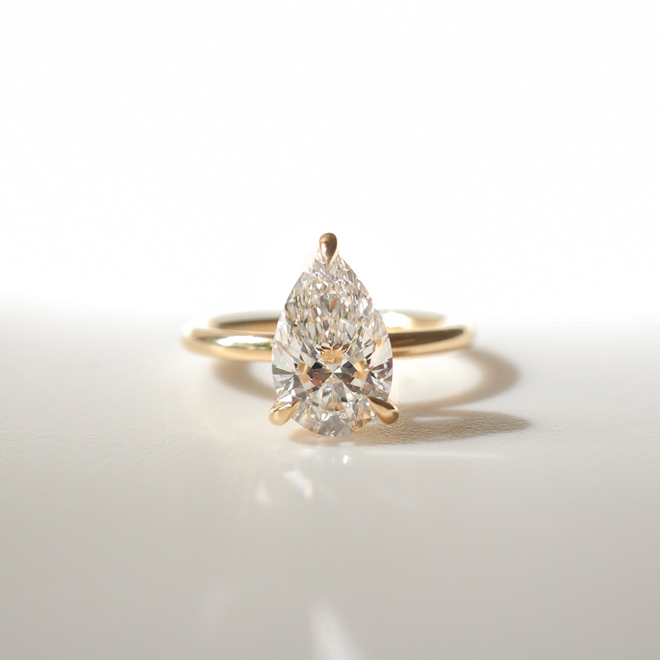 Gold ring with a pear-shaped diamond centerpiece, elegantly showcased on a light background. Perfect for luxury jewellery enthusiasts.