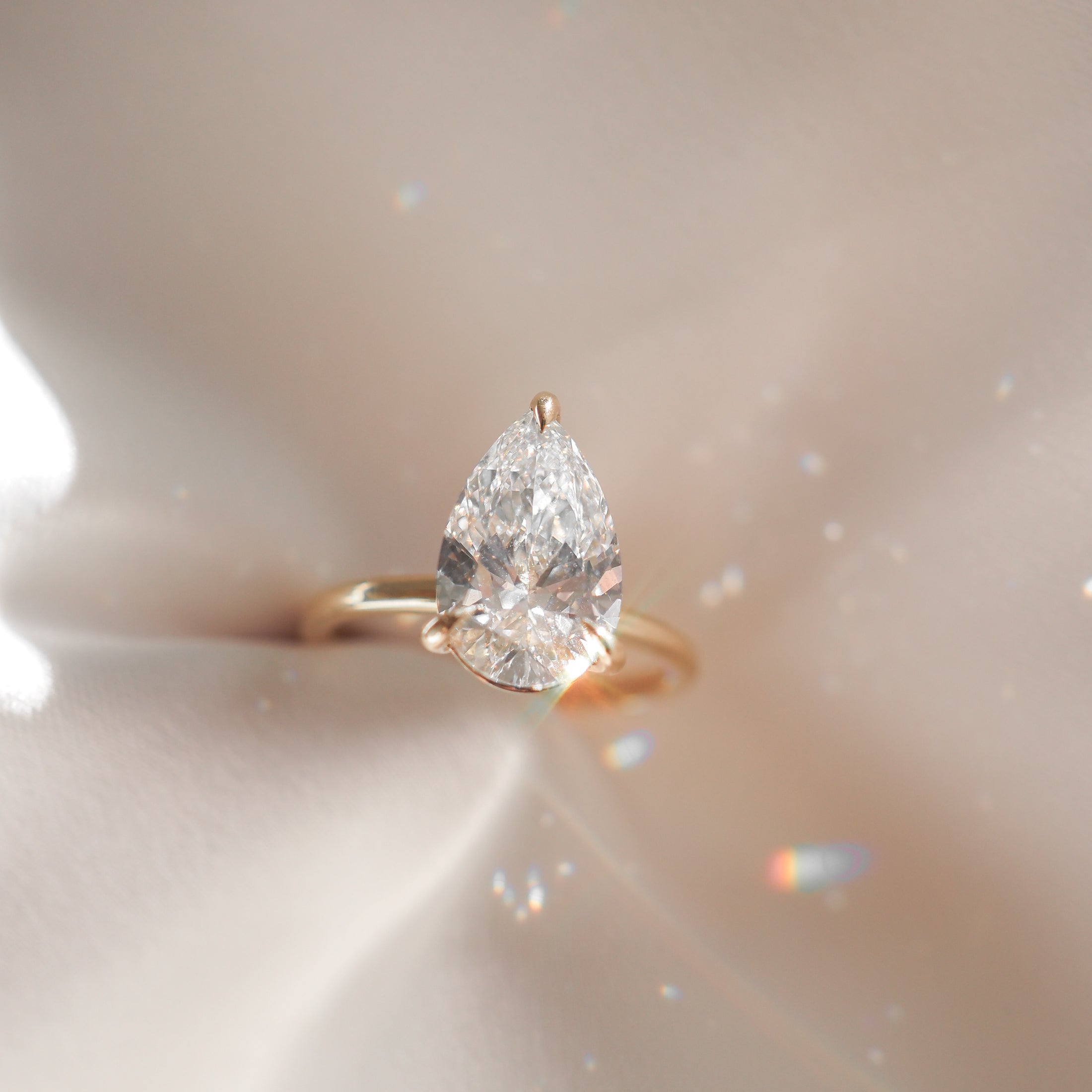 Pear-cut diamond ring with gold band on silky fabric, showcasing luxury jewellery sparkle and elegance.