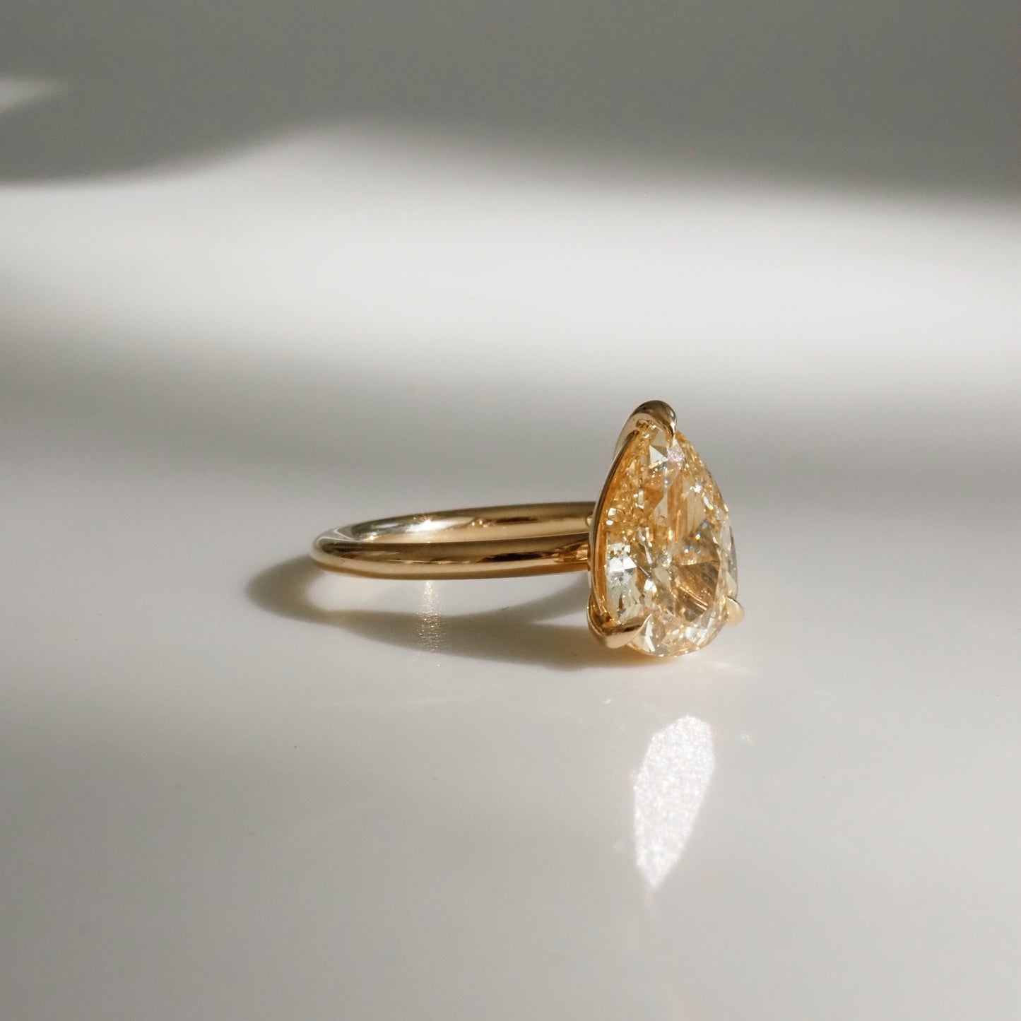 Gold ring with a pear-shaped diamond, reflecting sunlight on a white surface. Elegant high-end jewellery.
