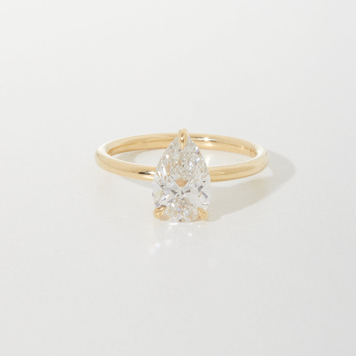 Gold ring with a pear-shaped diamond set in a minimalist band, reflecting elegance and luxury on a light background.