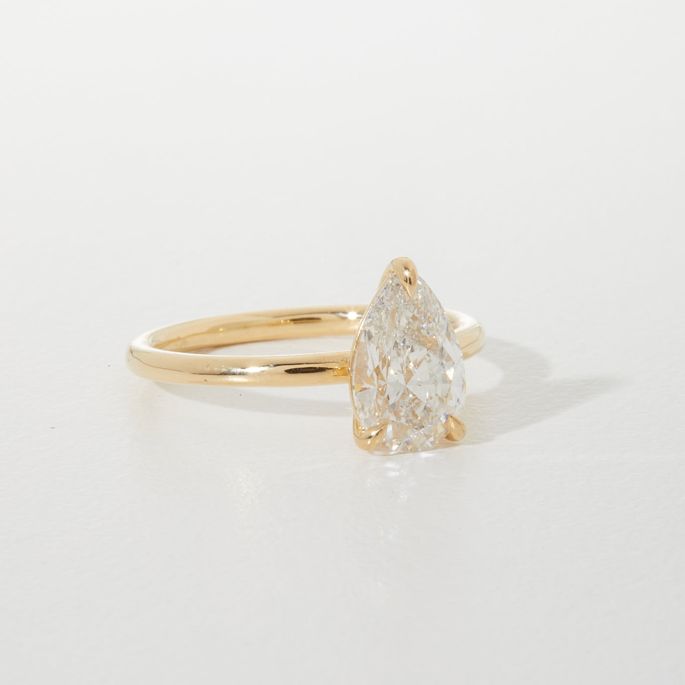Gold ring with a large, pear-shaped diamond set on a minimalist band, elegantly displayed on a soft white background.