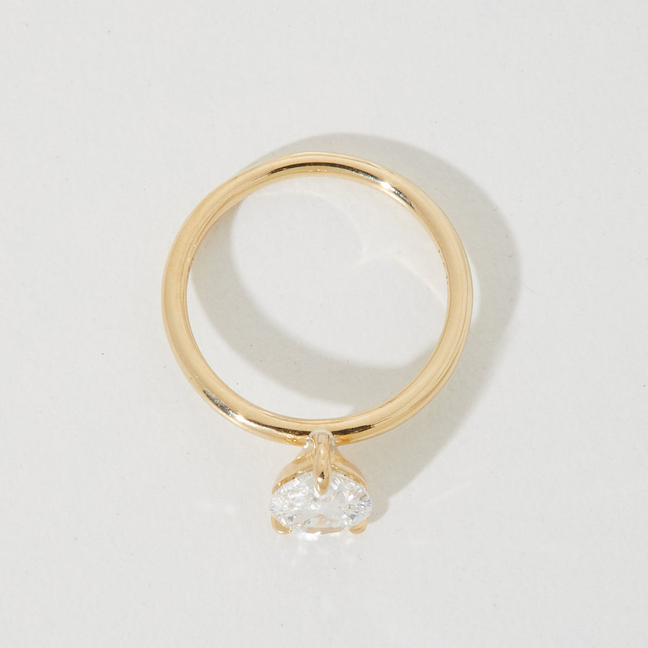 Elegant gold engagement ring featuring a sparkling heart-shaped diamond solitaire, casting a soft shadow on a light background.