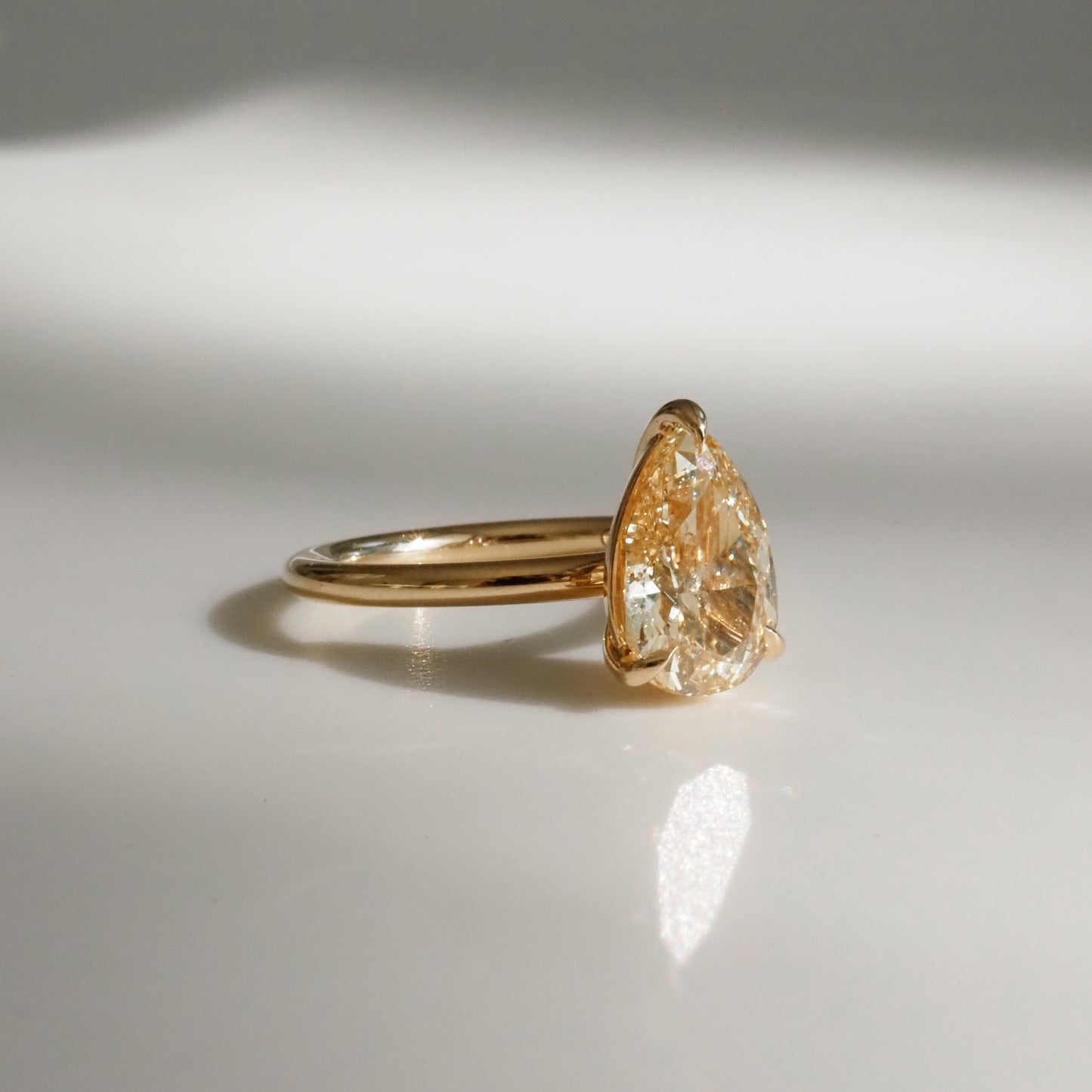 Gold ring featuring a pear-shaped diamond, elegantly reflecting light on a smooth surface. Perfect luxury jewellery piece.