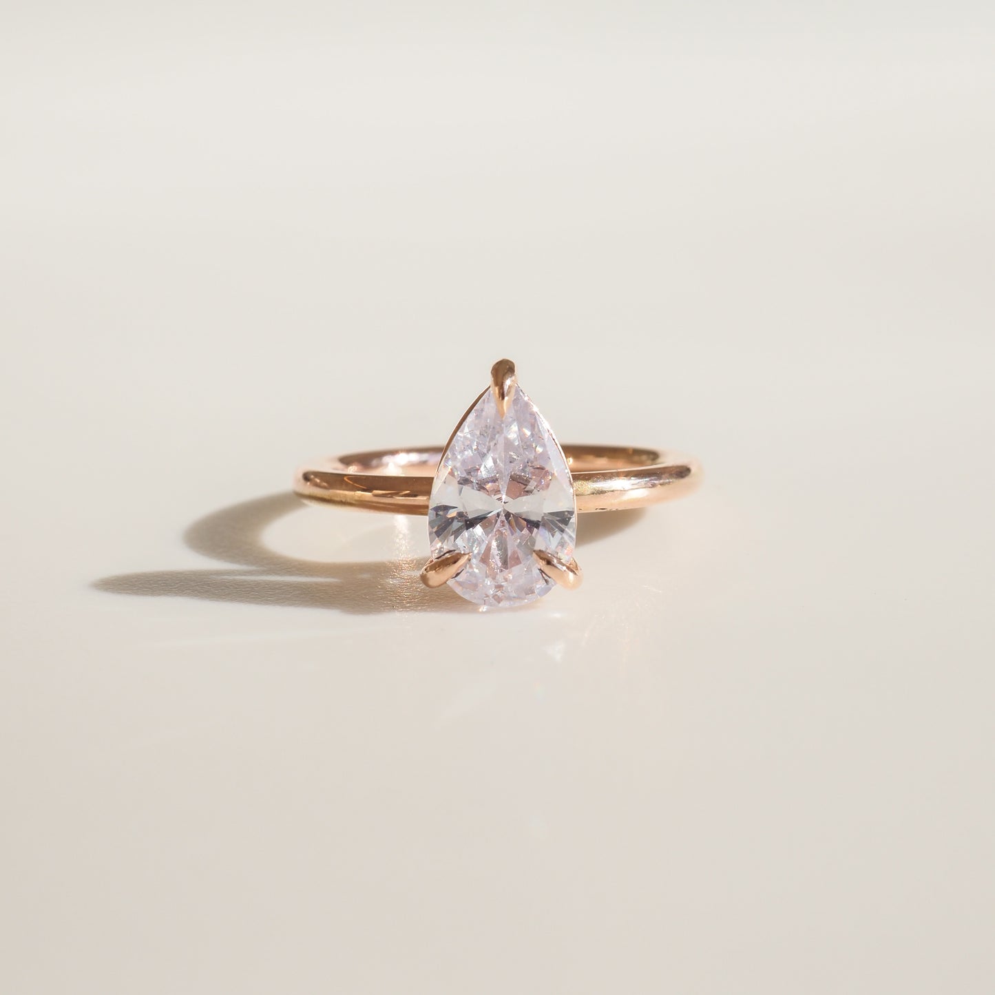 Pear-shaped diamond ring set in elegant rose gold band, displayed on a smooth surface with soft lighting.