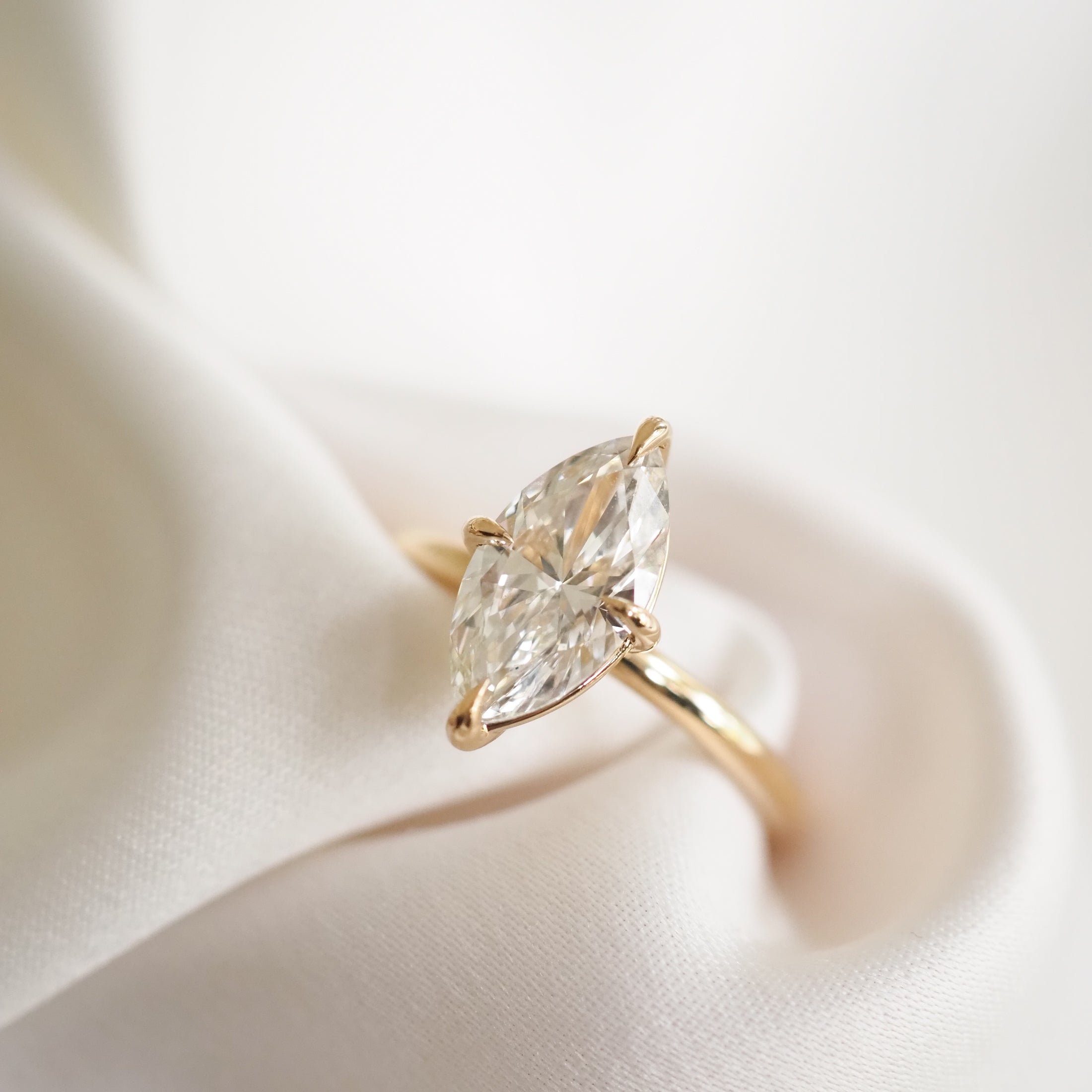 Elegant marquise-cut diamond ring on silky fabric; luxury jewellery with gold band, perfect for engagements or special occasions.