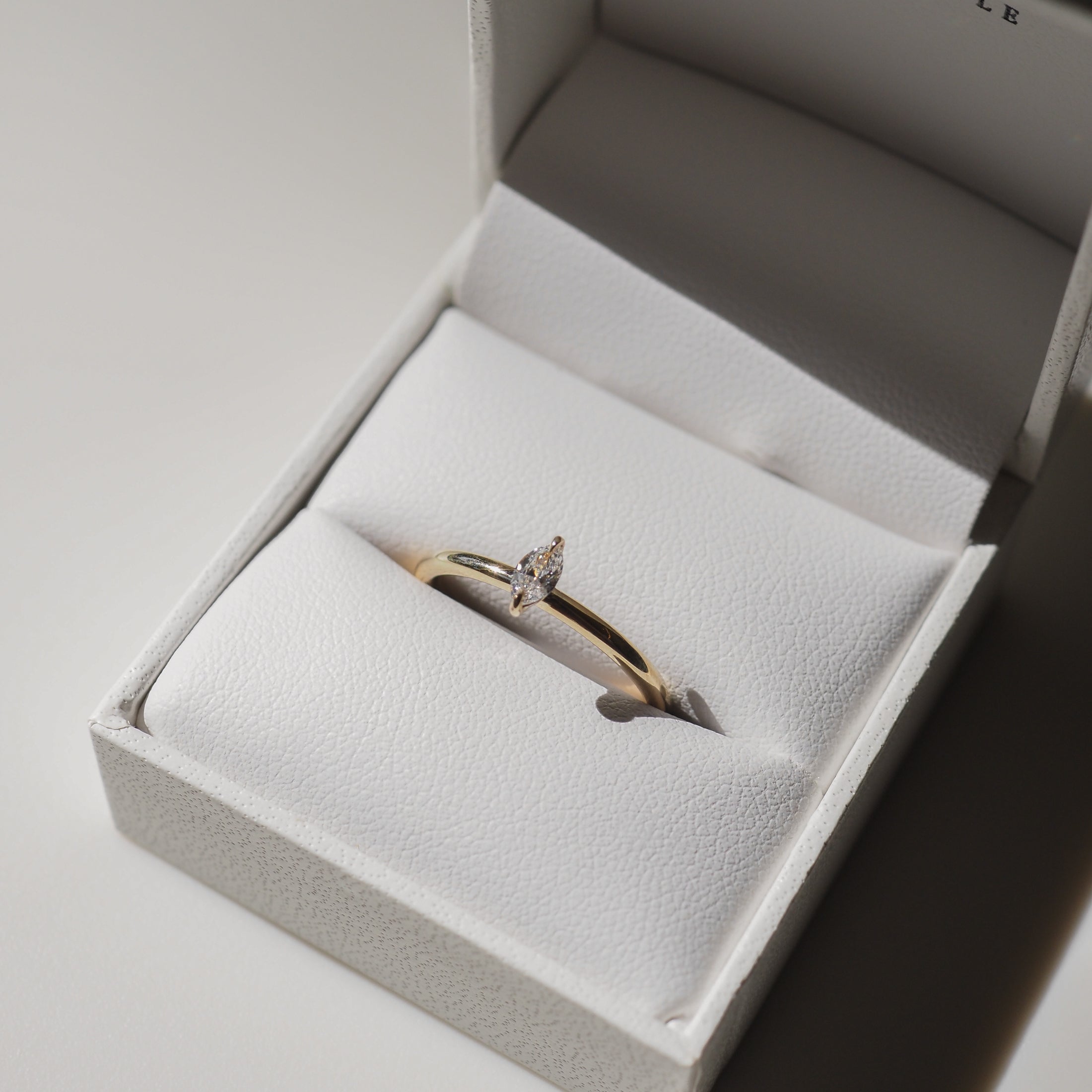 Elegant gold ring with a marquise diamond displayed in a white, open jewellery box, reflecting luxury.