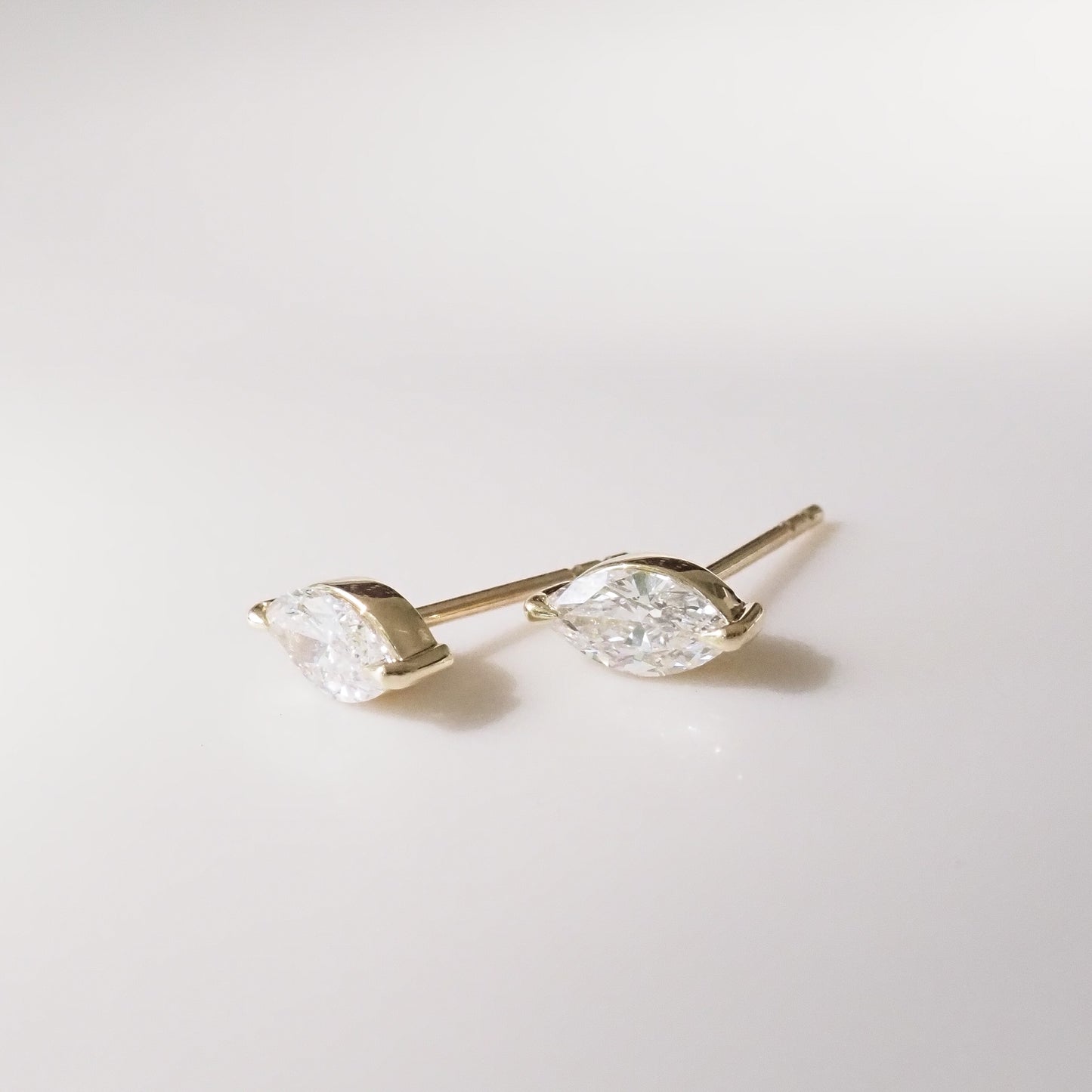 Pair of gold marquise earrings with clear gemstones on a light gray background