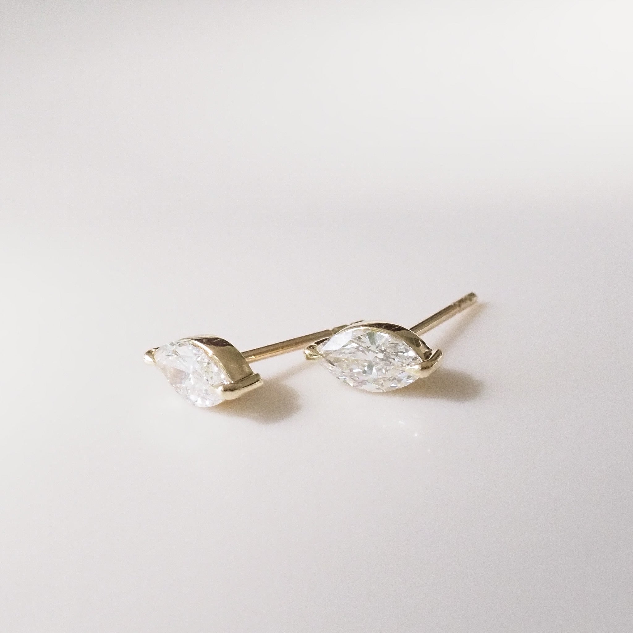 Pair of gold marquise earrings with clear gemstones on a light gray background
